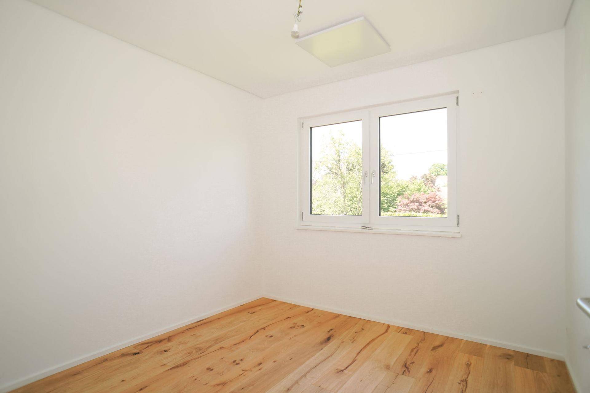 Geräumiges Schlafzimmer mit Holzboden und einem großen Fenster, das den Raum erhellt.