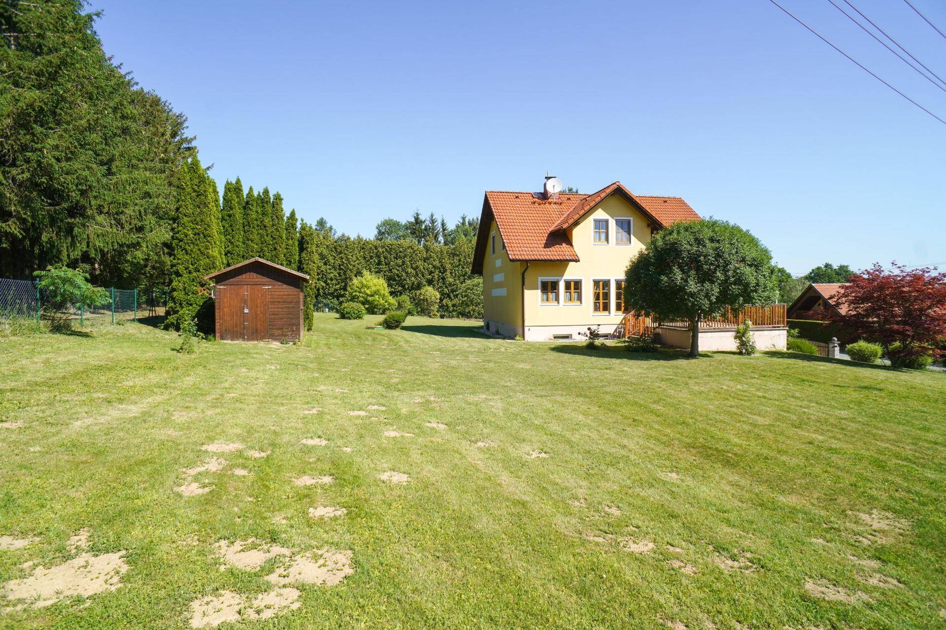 Einfamilienhaus mit großem Garten und einem Holzschuppen, umgeben von viel Grün.