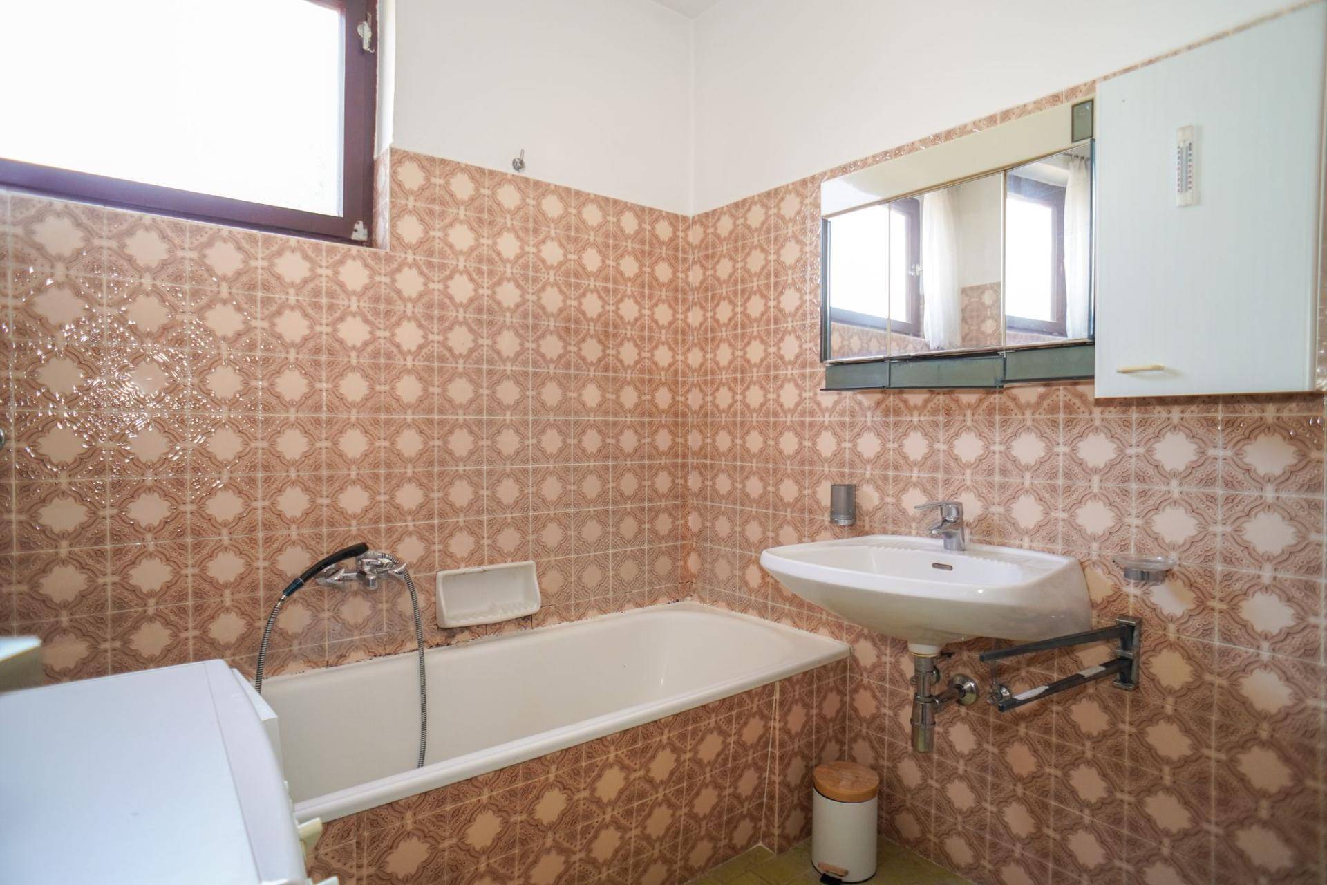 Badezimmer im 80er-Jahre-Stil mit Badewanne, Waschbecken und gemusterten Fliesen.