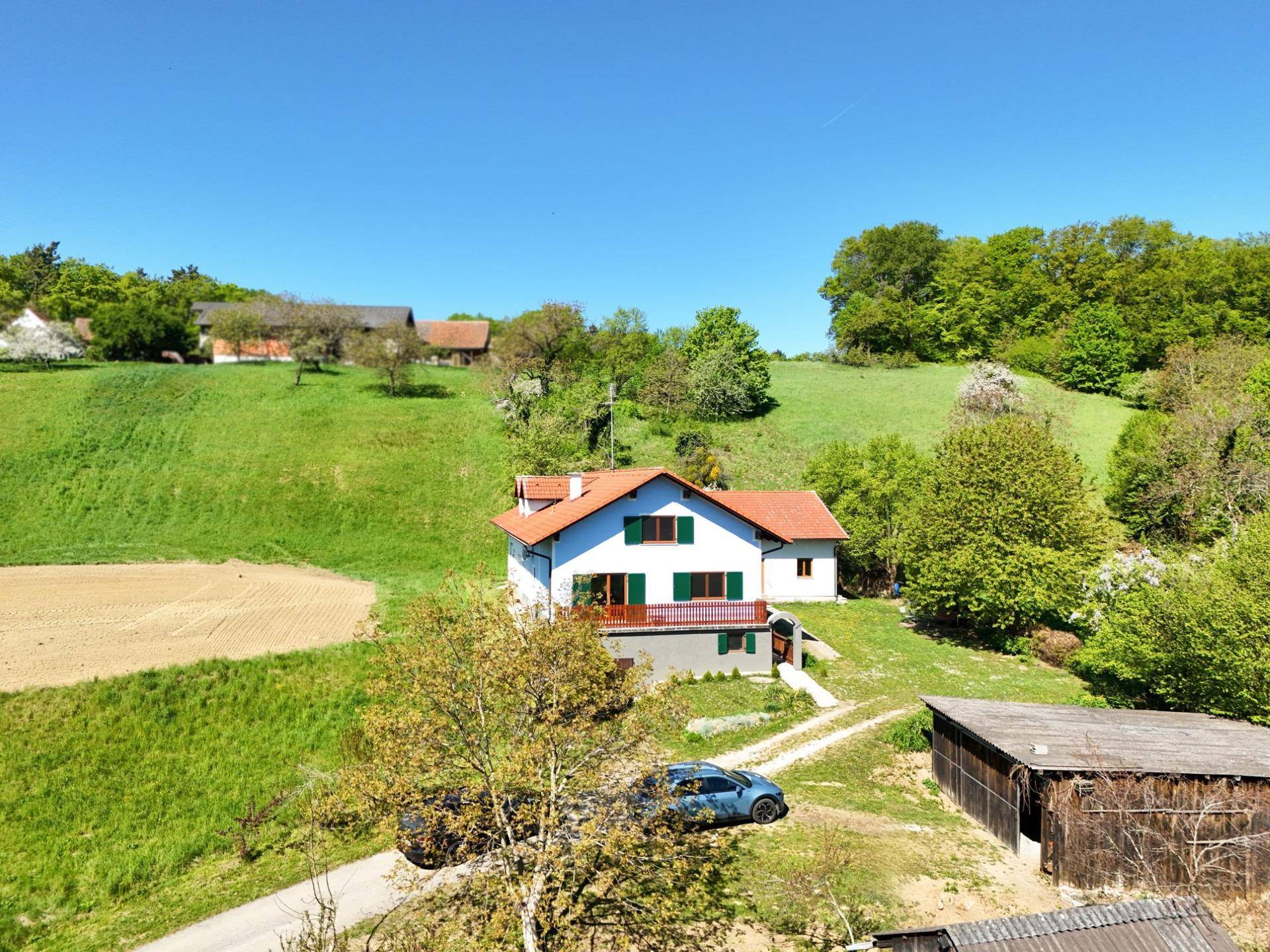 Luftaufnahme eines Hauses mit Nebengebäuden in einer weitläufigen grünen Landschaft, sonniger Tag.