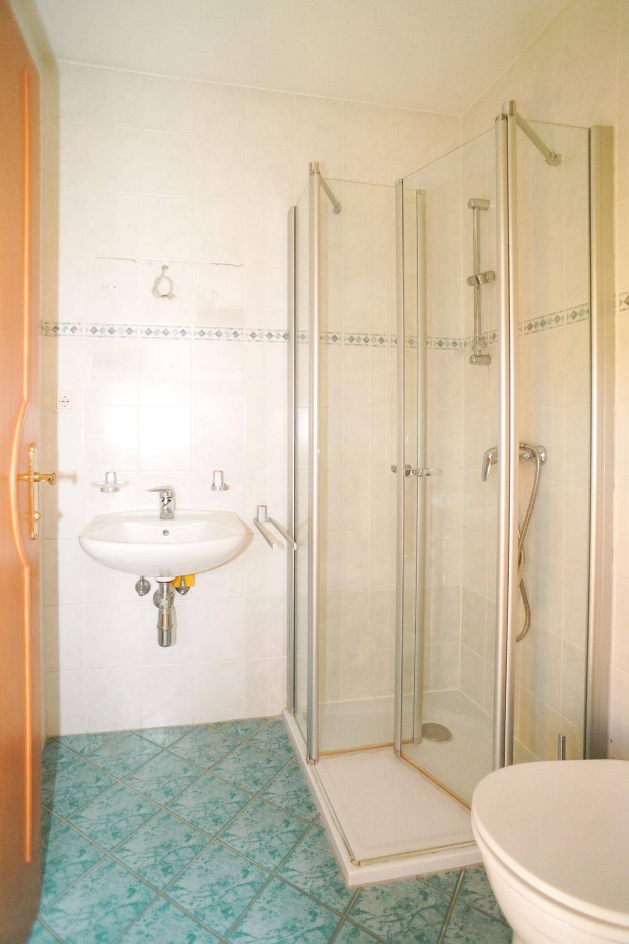 Badezimmer mit Duschkabine, Waschbecken und WC, ausgestattet mit hellen Wand- und grünen Bodenfliesen.