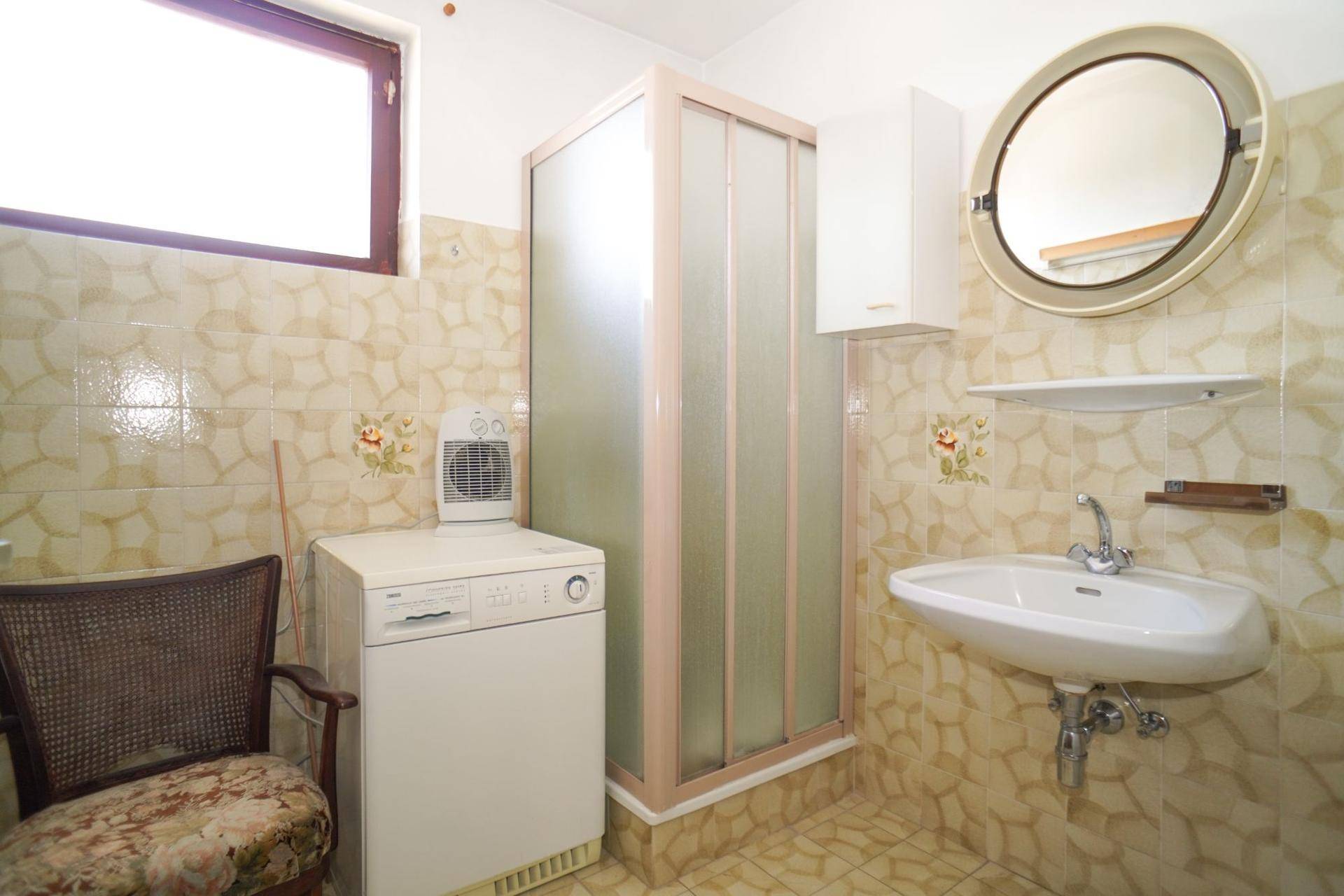 Badezimmer im 80er-Jahre-Stil mit Dusche, Waschbecken und gemusterten Fliesen.