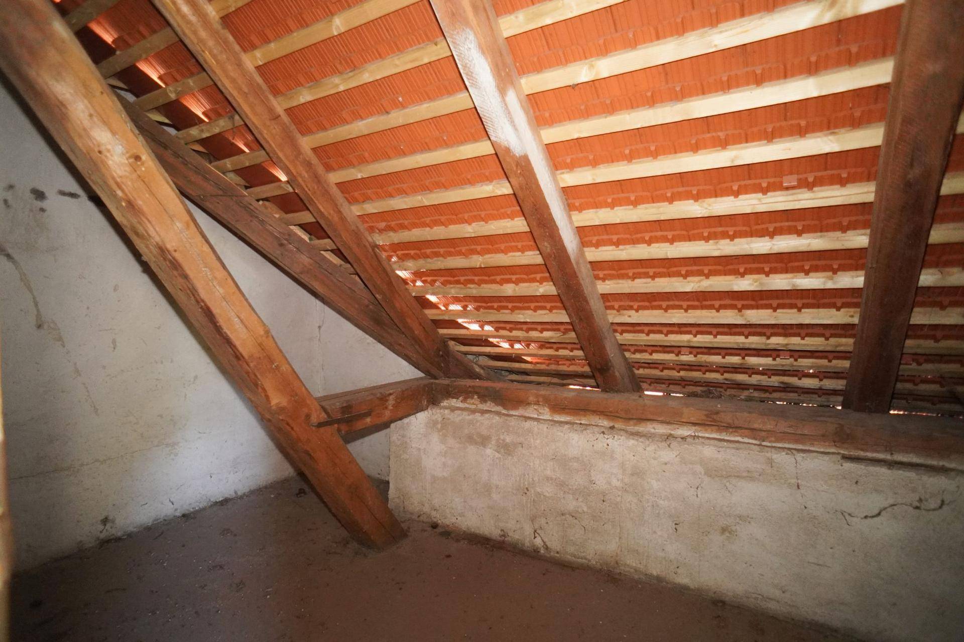 Dachboden mit sichtbaren Holzbalken und Ziegeln, der Ausbaupotenzial bietet.