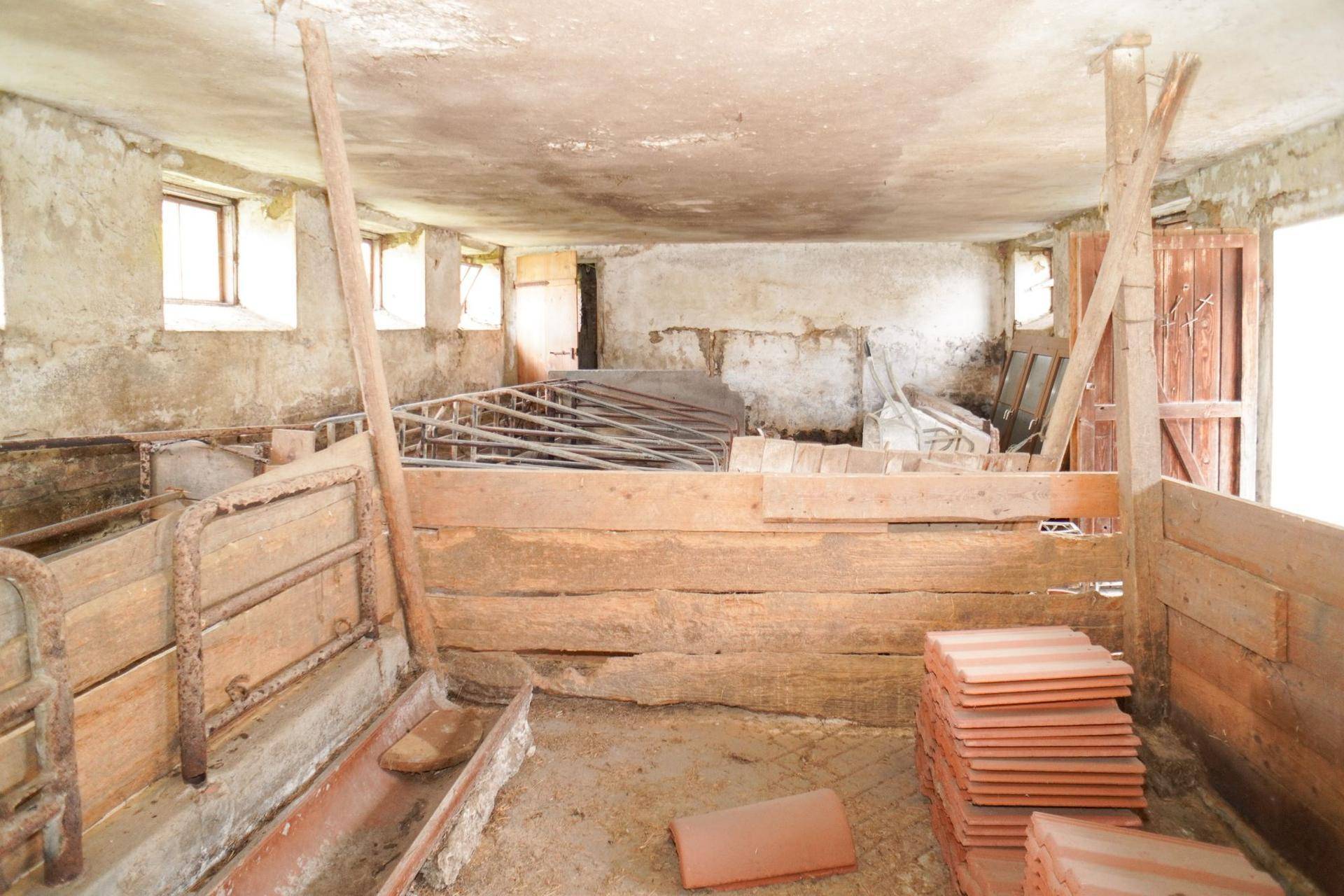 Rustikaler Innenraum eines Stalls mit Holzbalken, alten Futtertrögen und Baumaterialien.