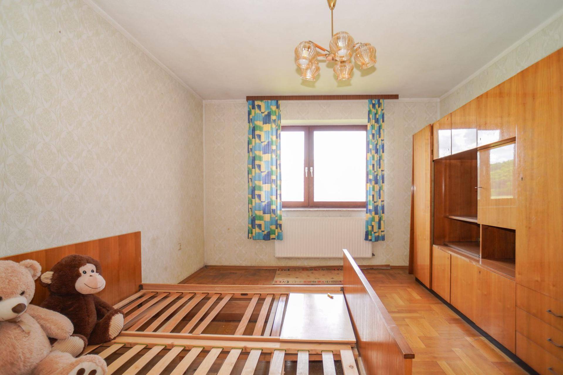 Kinderzimmer mit Holzdielenboden, Holzmöbeln und einem Fenster mit bunten Vorhängen.