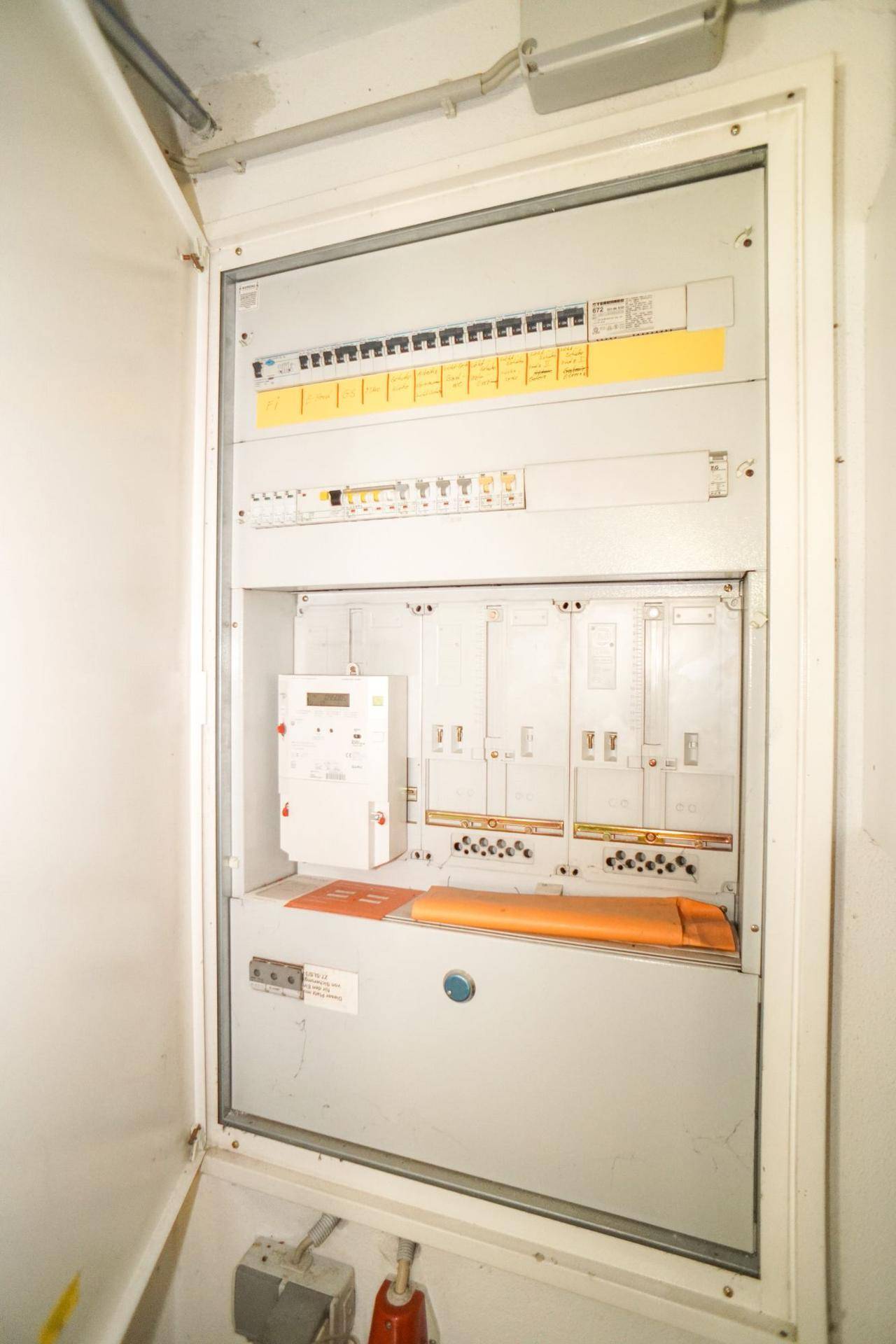 Offener Sicherungskasten mit elektrischen Installationen und Zählern in einem Technikraum.