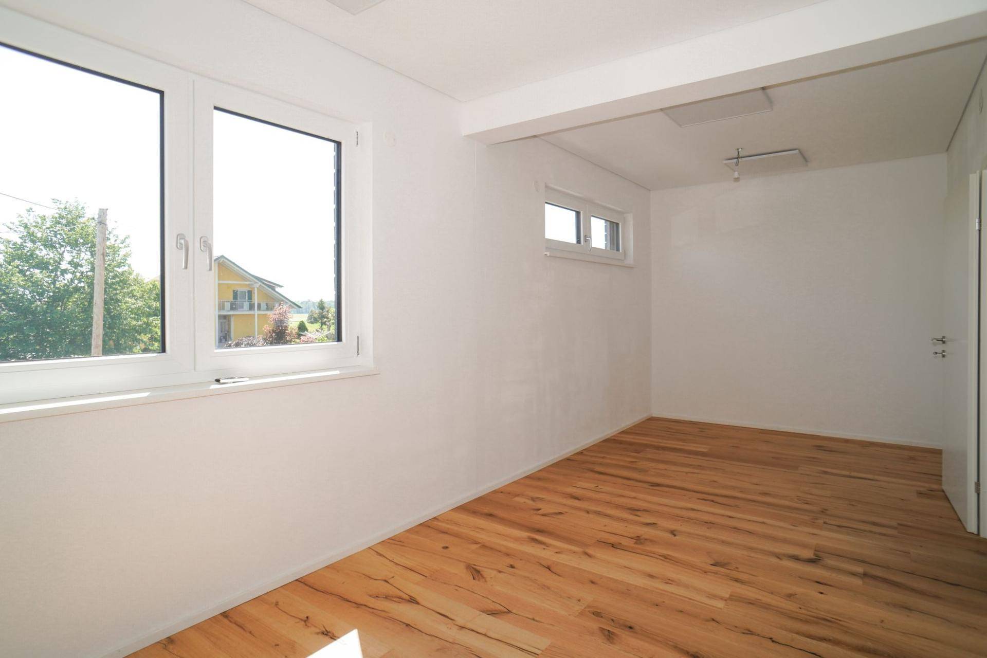 Helles Schlafzimmer mit Holzboden und Fenstern, die einen weiten Blick in die Umgebung bieten.