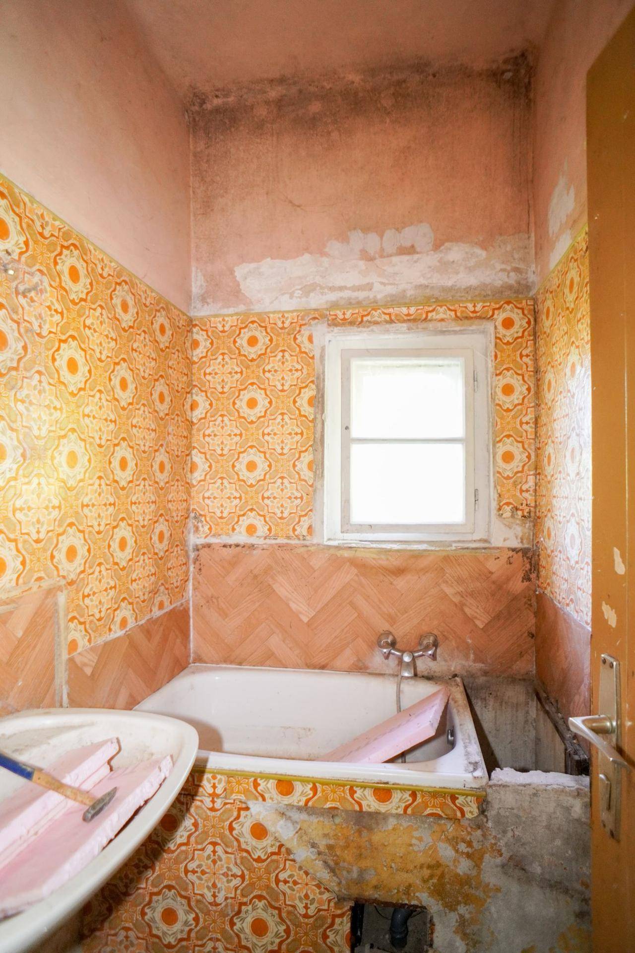 Badezimmer mit orangefarbenen Fliesen, Badewanne und Fenster, das umfassende Renovierung erfordert.