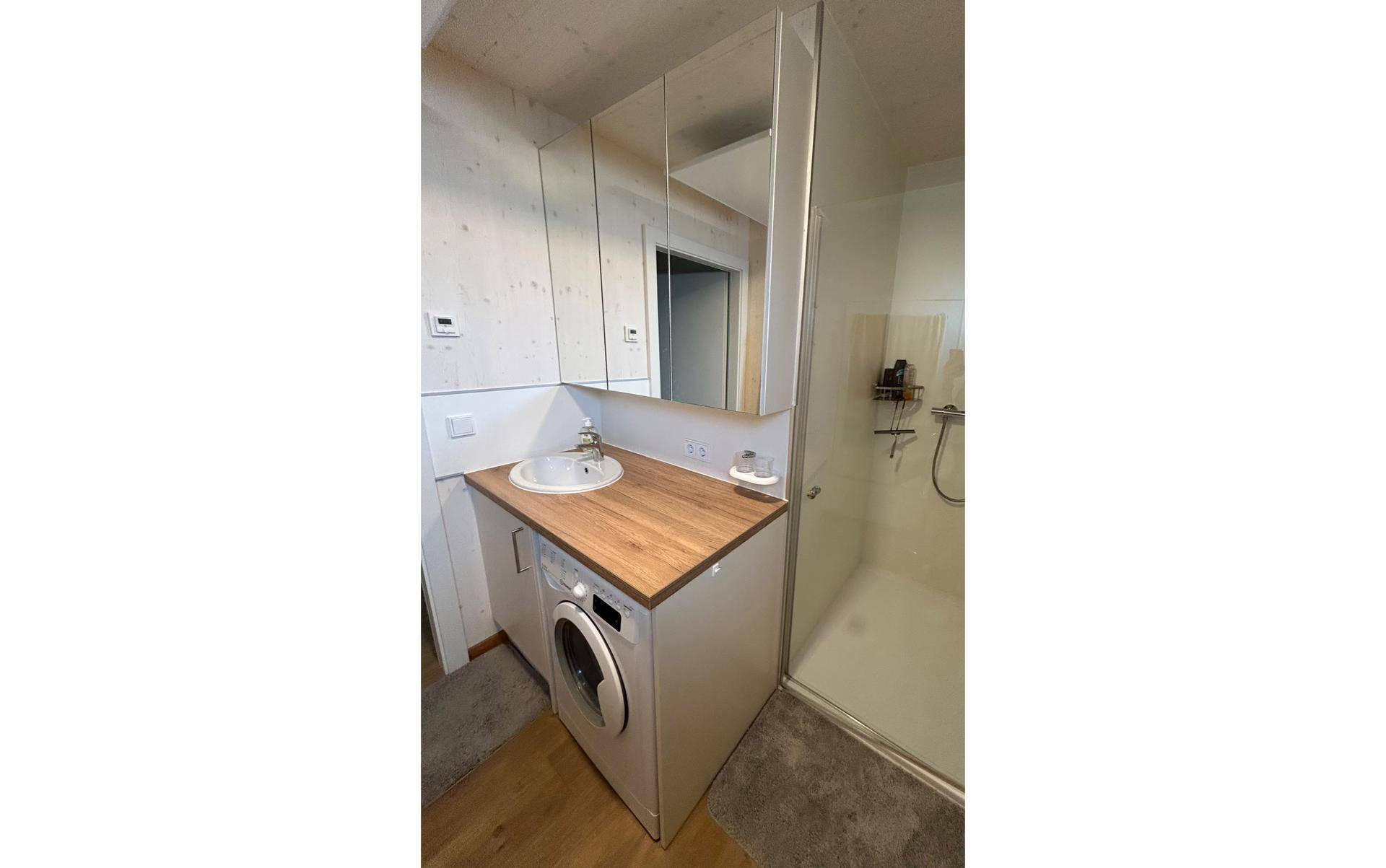 Modernes Badezimmer mit Waschmaschine, Holzwaschtisch und begehbarer Dusche.