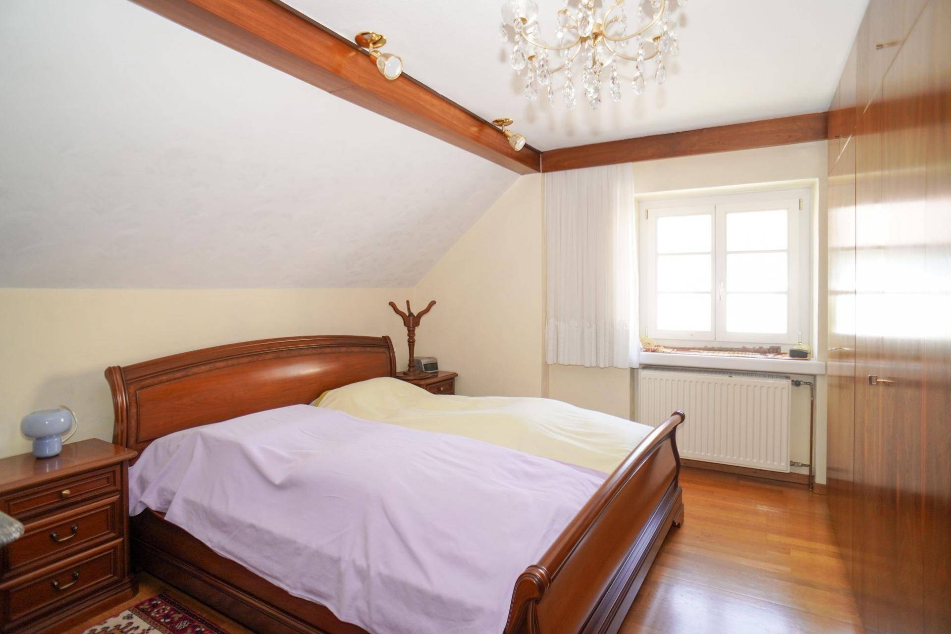 Schlafzimmer im Dachgeschoss mit Holzbalken, Doppelbett und Fenster für natürliches Licht.