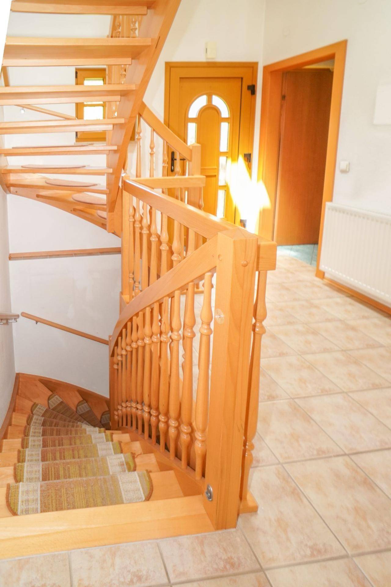 Holztreppe mit Teppichläufer, die in das Obergeschoss führt, in einem hellen Eingangsbereich.