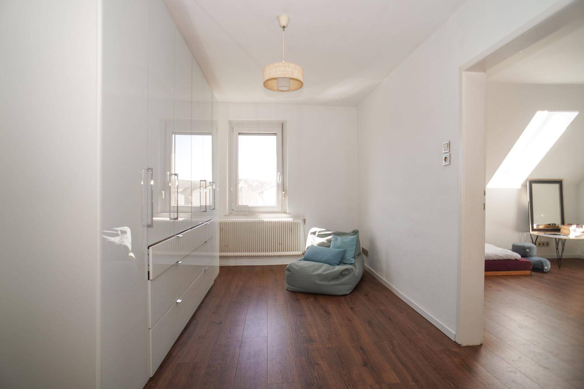 Heller Flur mit glänzenden Einbauschränken und Holzboden, der zu einem Zimmer mit Dachschräge führt.