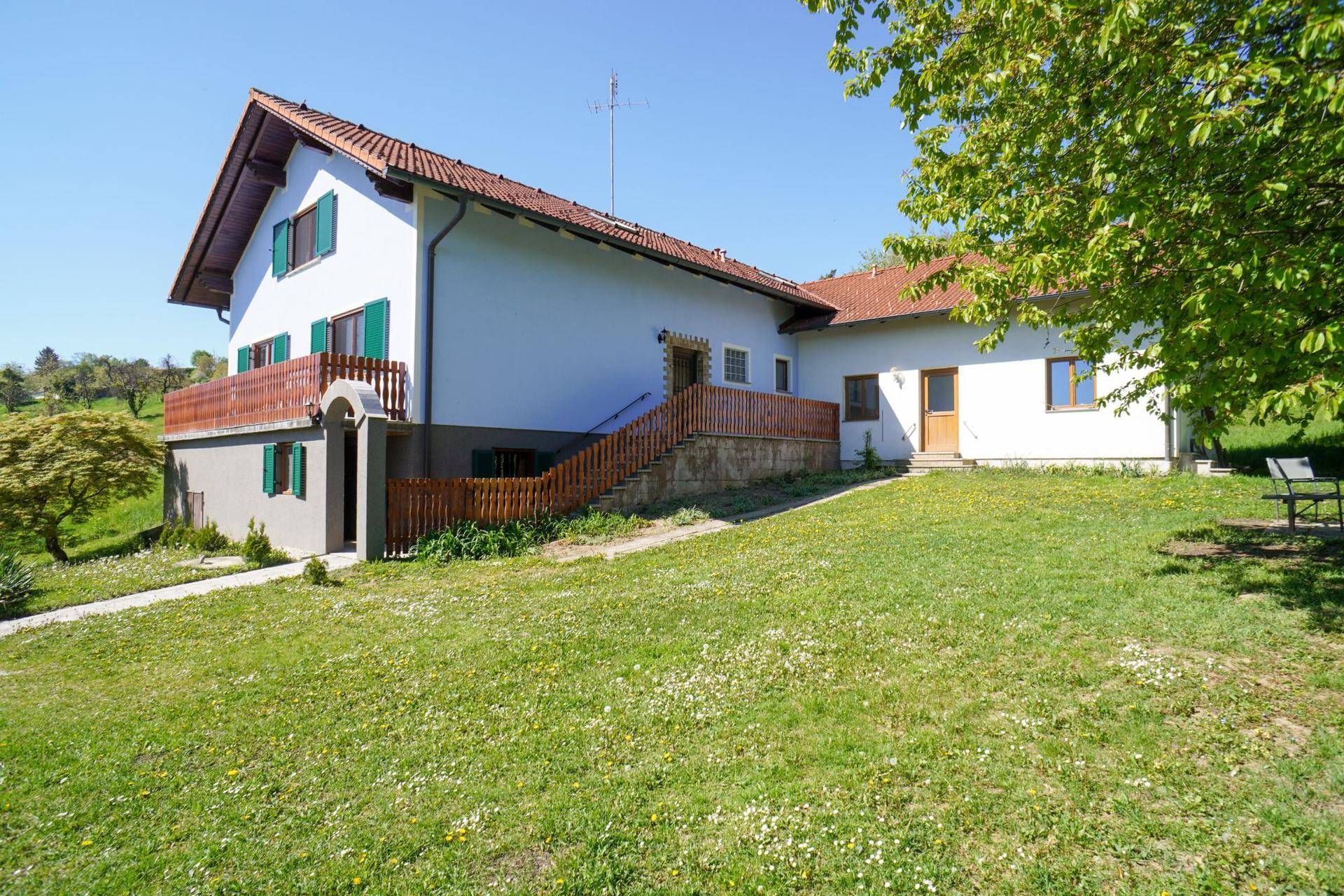 Ländliches Haus mit rotem Ziegeldach, grünen Fensterläden und großem Gartenbereich.
