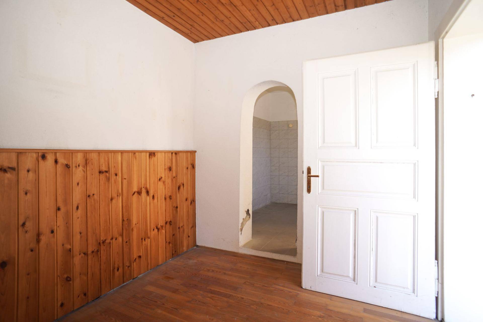 Innenraum mit Holzvertäfelung, Holzboden und einer Tür, die zu einem gefliesten Bereich führt.