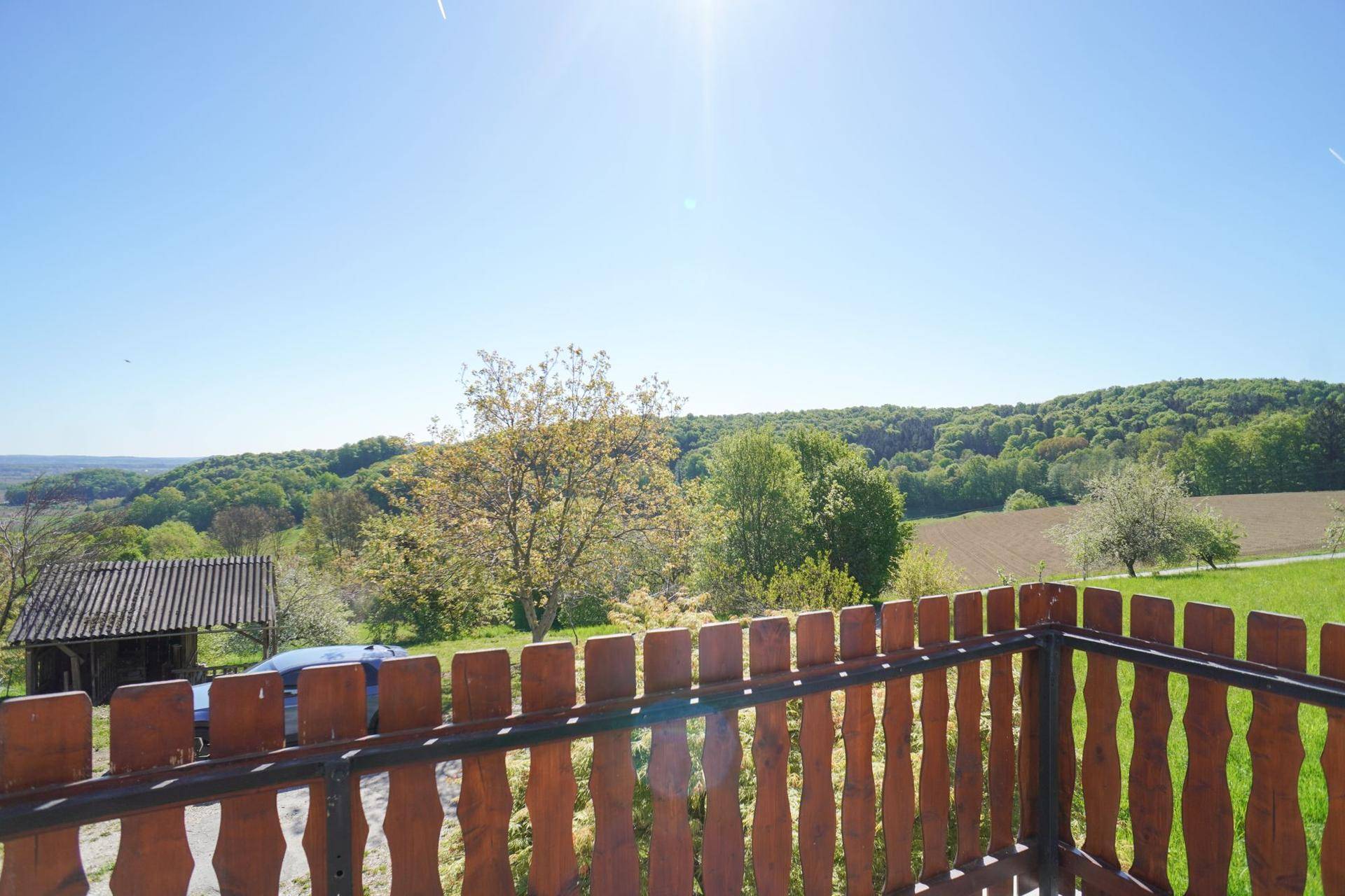 Sonniger Balkon mit Holzzaun und Panoramablick auf die umliegende Natur.