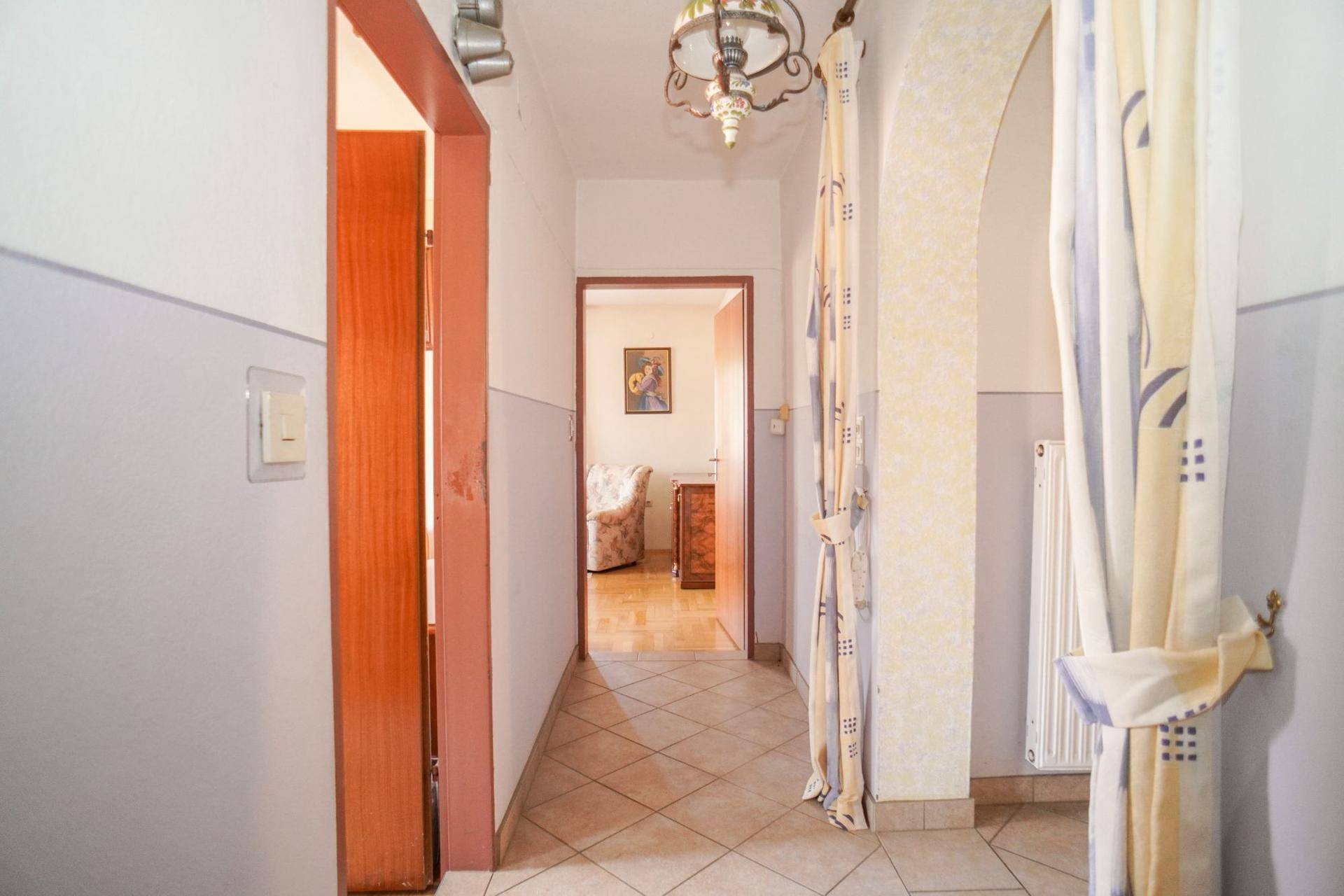 Langer Flur mit Fliesenboden, hellen Wänden und einem Blick in angrenzende Zimmer.