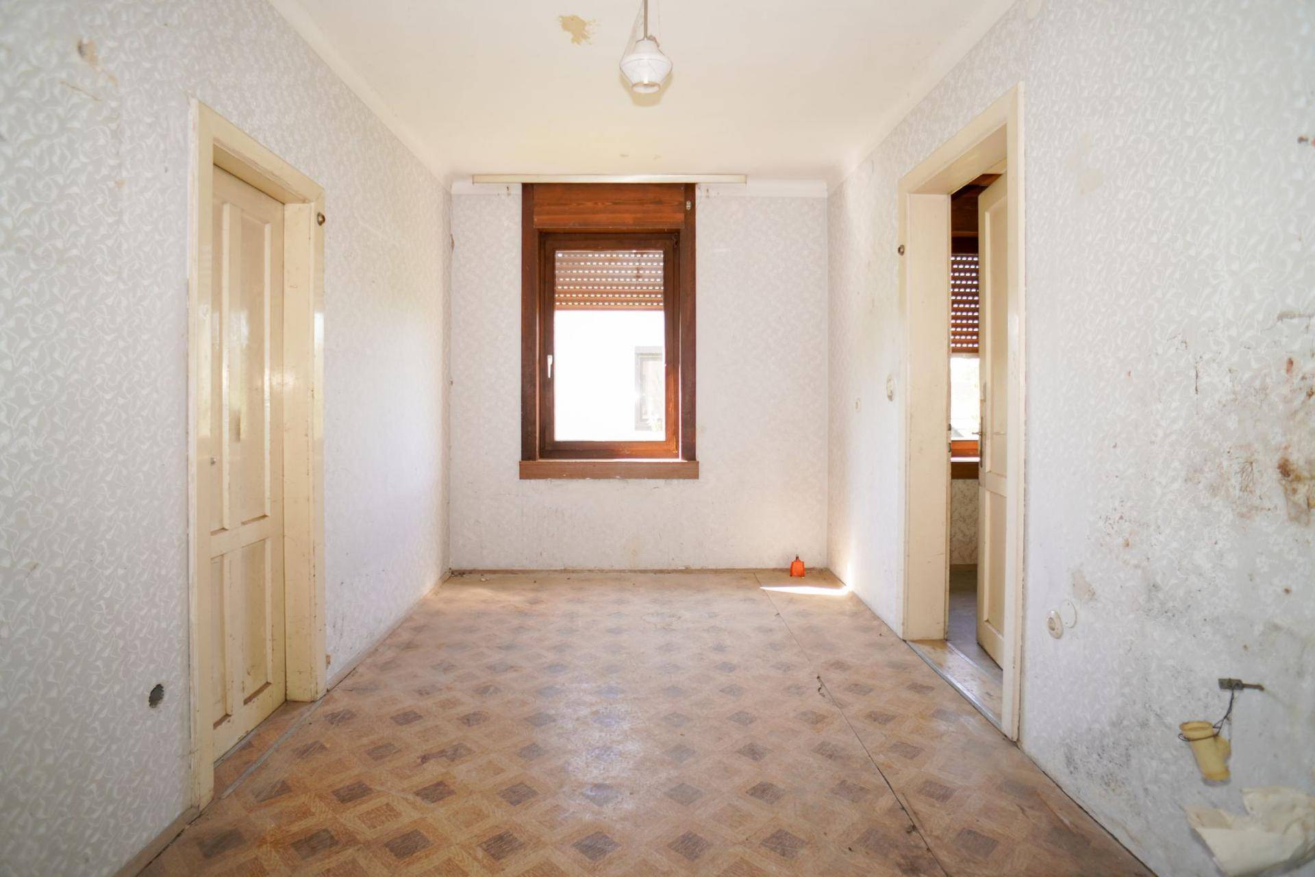 Heller Raum mit Linoleumboden und Fenster, das auf Renovierungsbedarf hindeutet.
