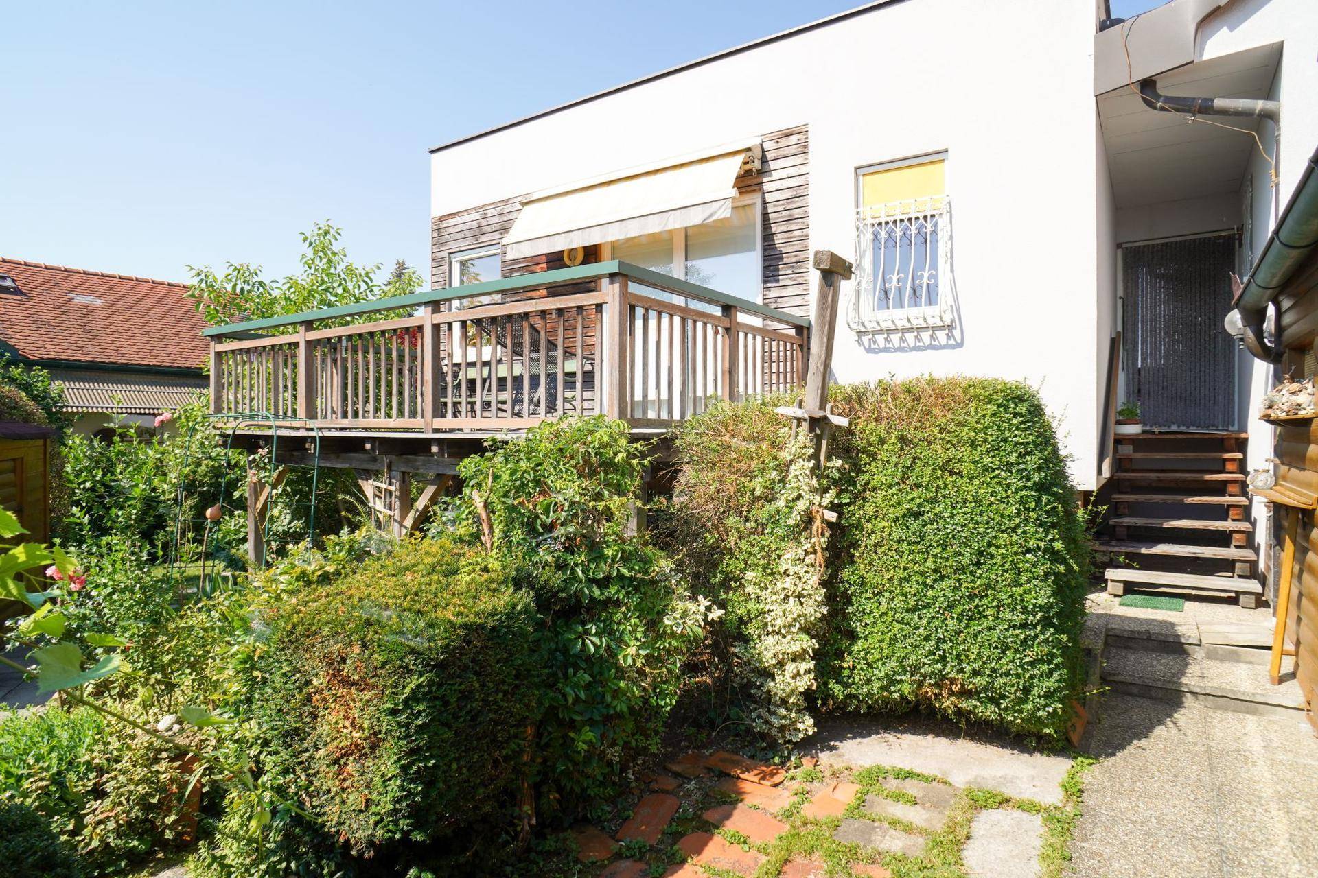 Gartenbereich mit üppiger Bepflanzung, Treppe und erhöhtem Balkon am Hauptgebäude.
