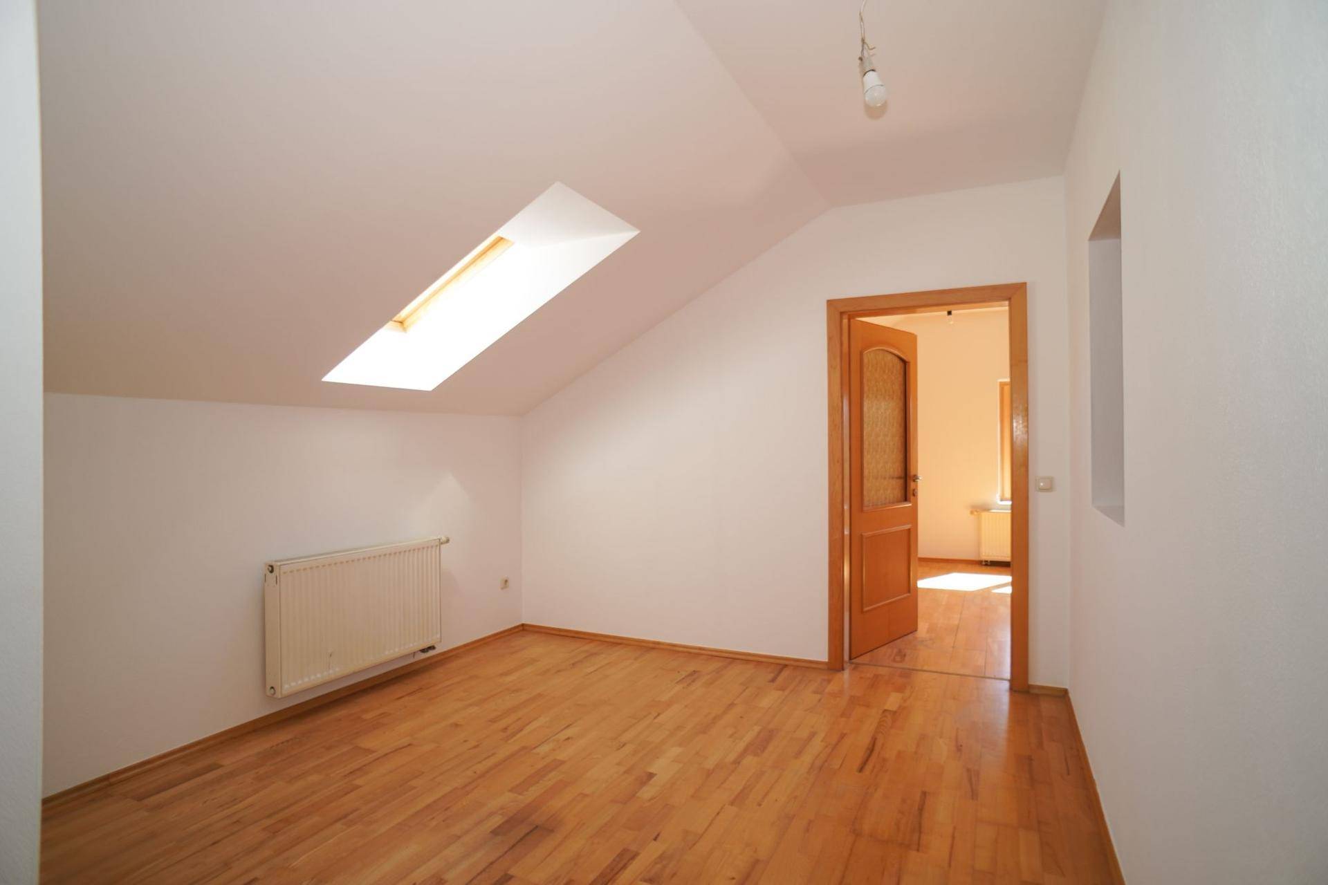 Helles Dachzimmer mit Holzboden, Dachfenster und schrägen Wänden.