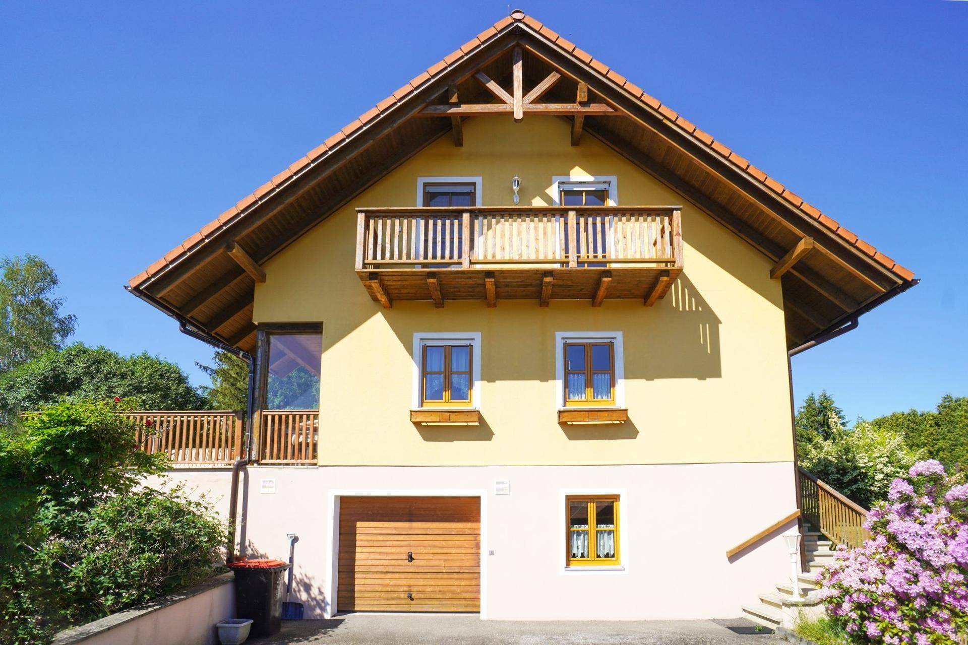 Fassade des Hauses mit Holzbalkon und integrierter Garage im Untergeschoss.