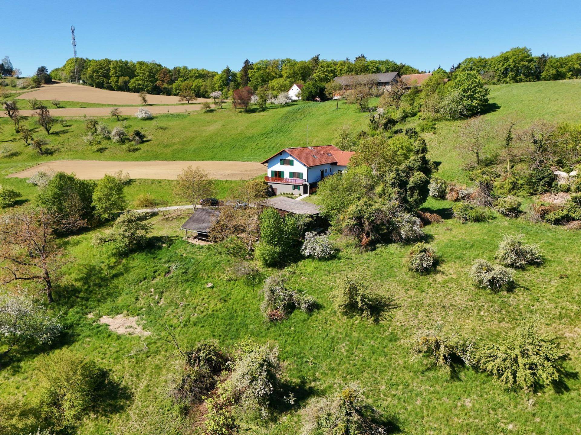 Panoramablick auf ein Haus eingebettet in eine grüne Hügellandschaft mit Bäumen und Feldern.
