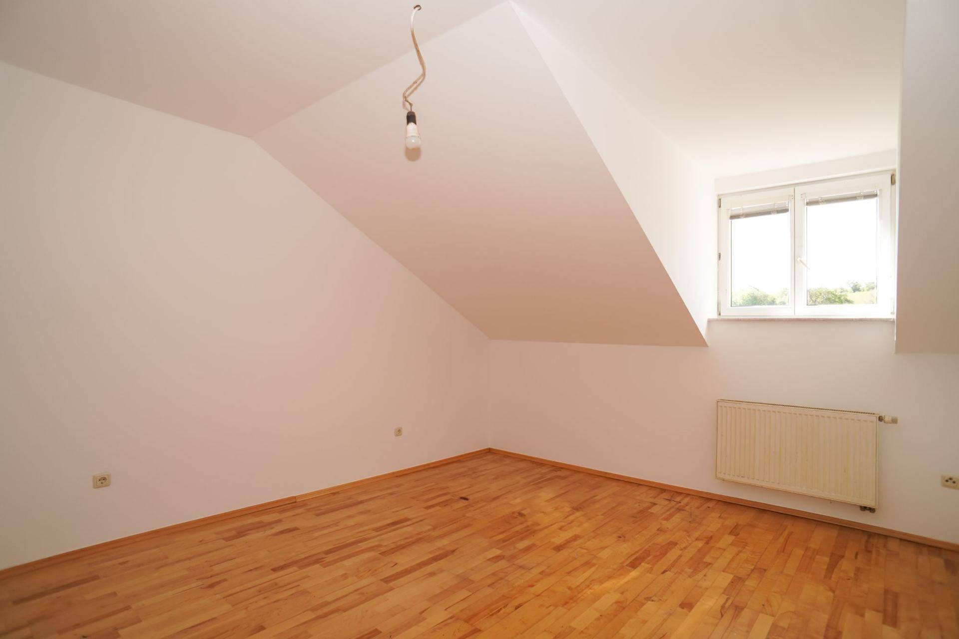 Dachzimmer mit Holzboden, Fenster und schrägen Wänden, ideal für ein gemütliches Schlafzimmer.