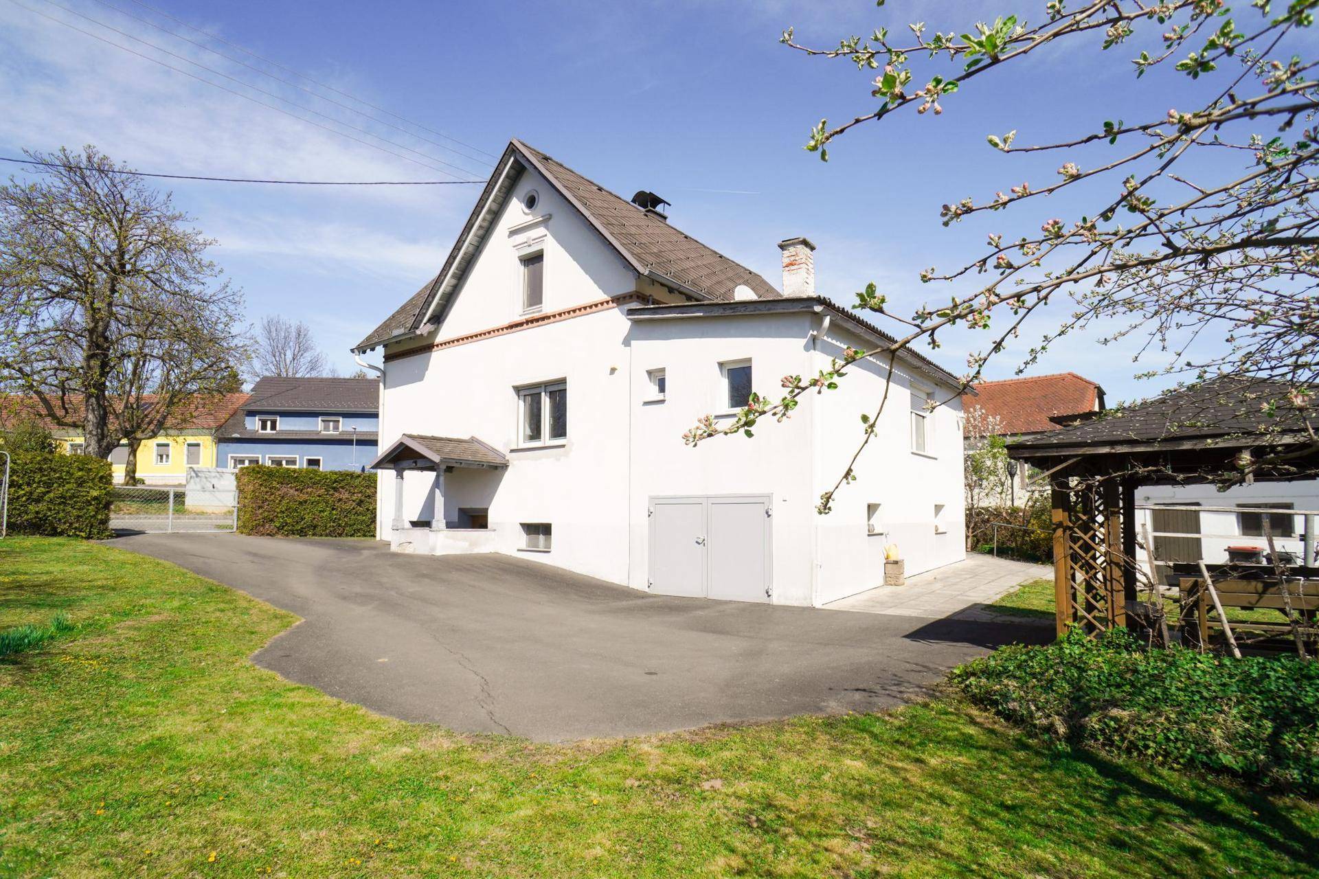 Weißes Einfamilienhaus mit Zufahrt und integrierter Garage, umgeben von Grünflächen.