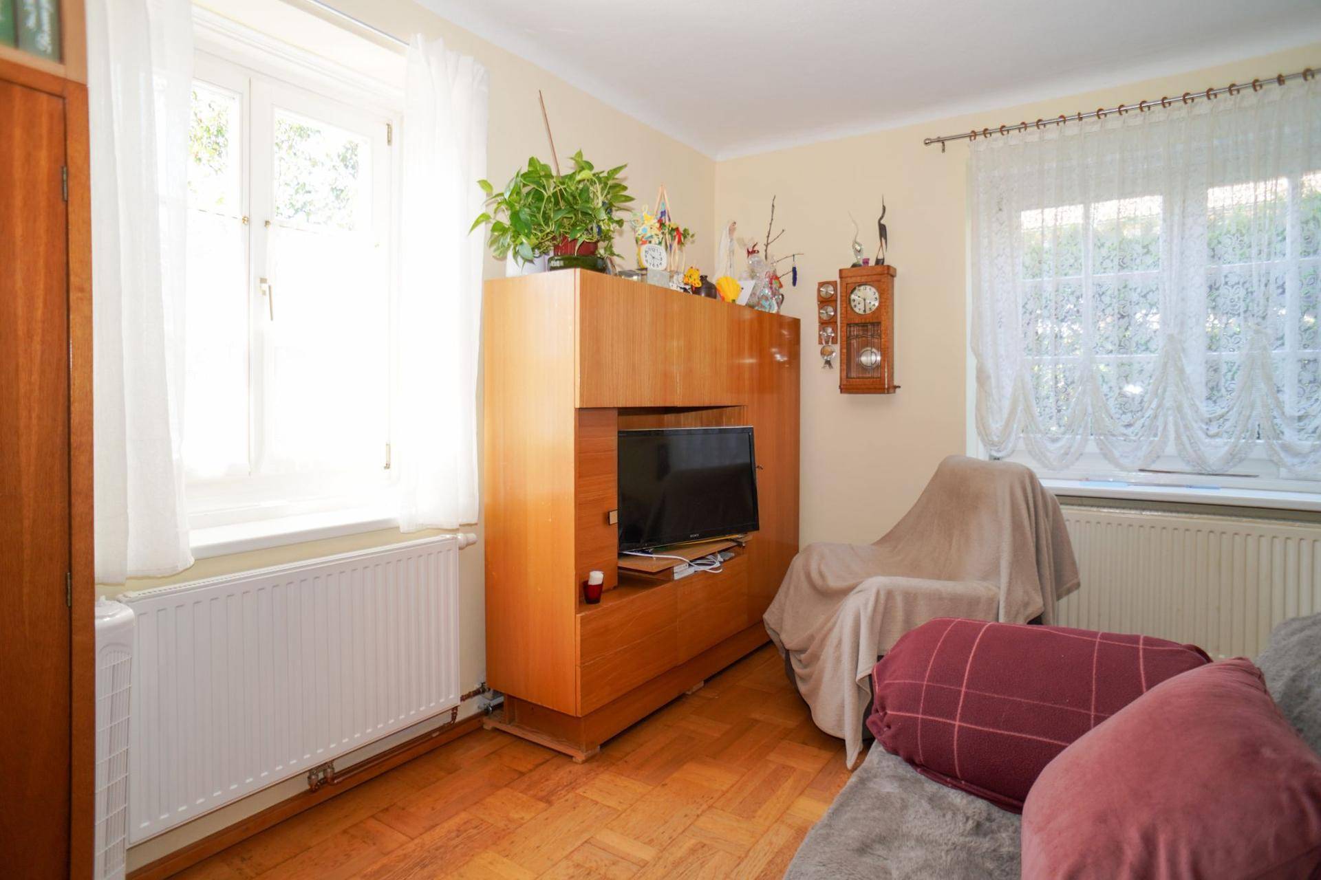 Gemütliches Wohnzimmer mit Holzboden, TV-Möbel und Blick ins Grüne durch die Fenster.