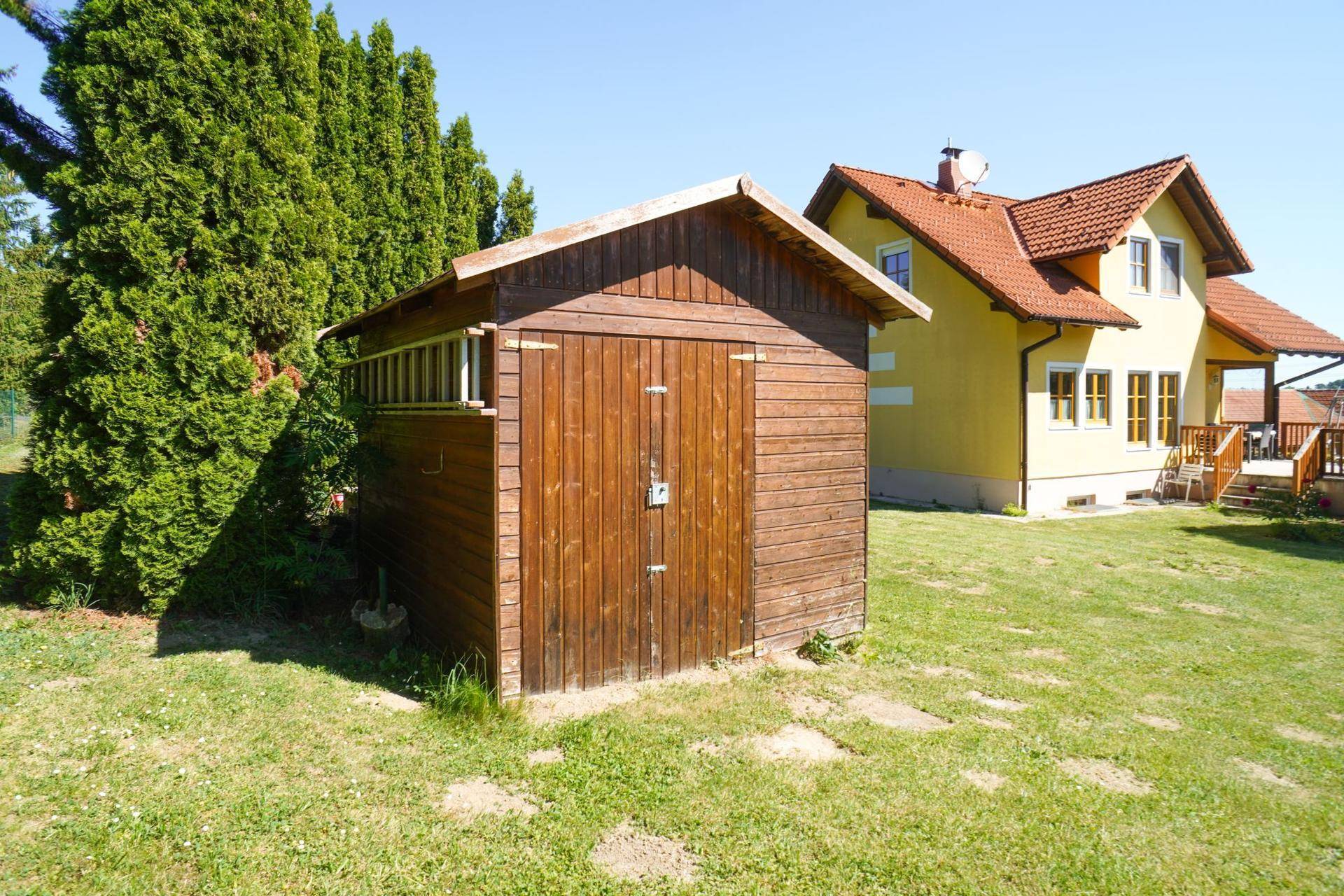 Rustikaler Holzschuppen im Garten neben dem gelben Wohnhaus, ideal für Gartengeräte.