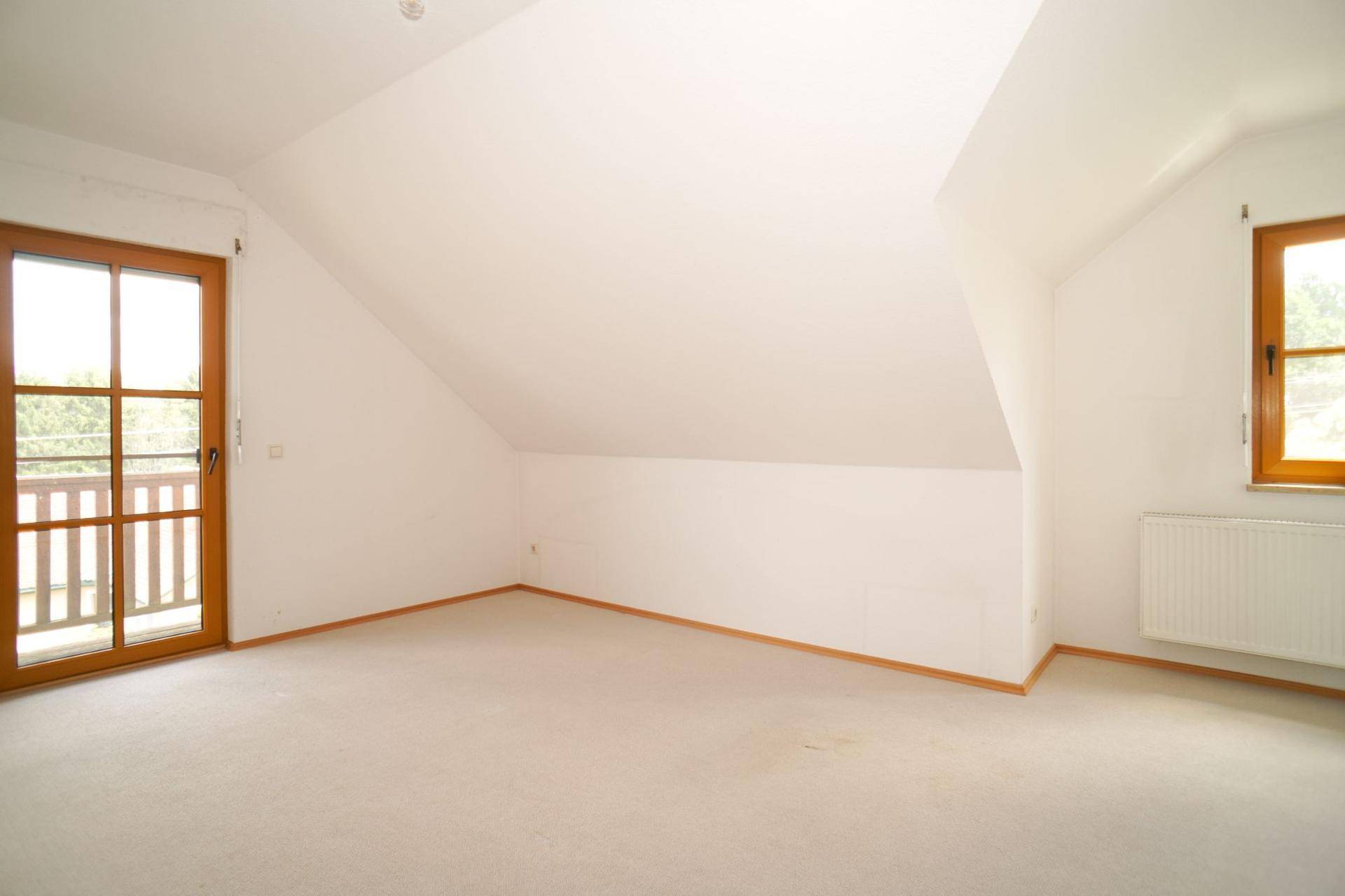 Helles Schlafzimmer im Dachgeschoss mit Teppichboden, Dachschräge und Zugang zu einem Balkon.