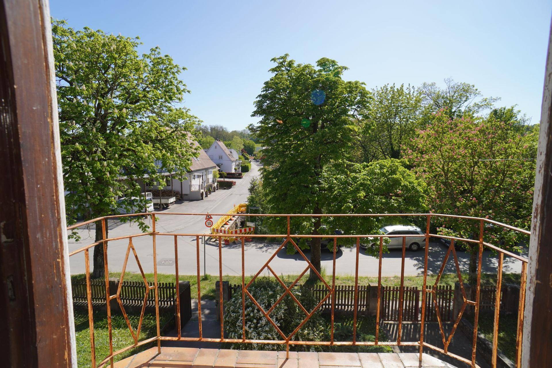 Kleiner Balkon mit schmiedeeisernem Geländer und Blick auf die Straße und Bäume.