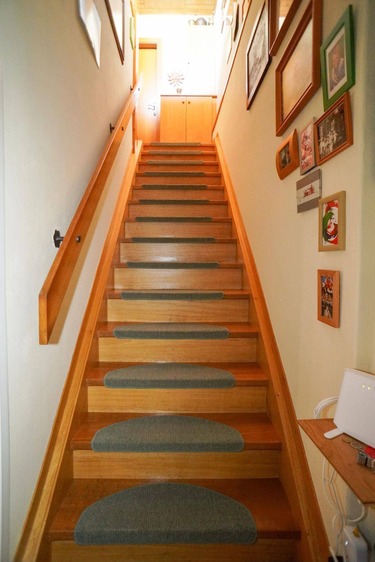 Holztreppe mit Teppichstufen und gerahmten Bildern an der hellen Wand.