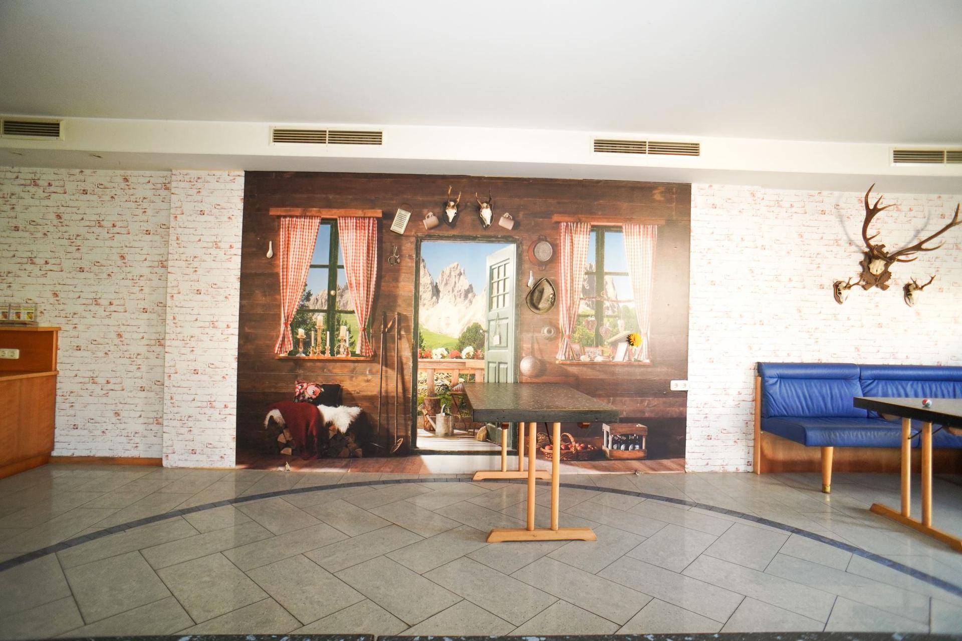 Großer Raum mit Wandgemälde im Alpenstil, Fliesenboden und traditionellen Dekorationen.