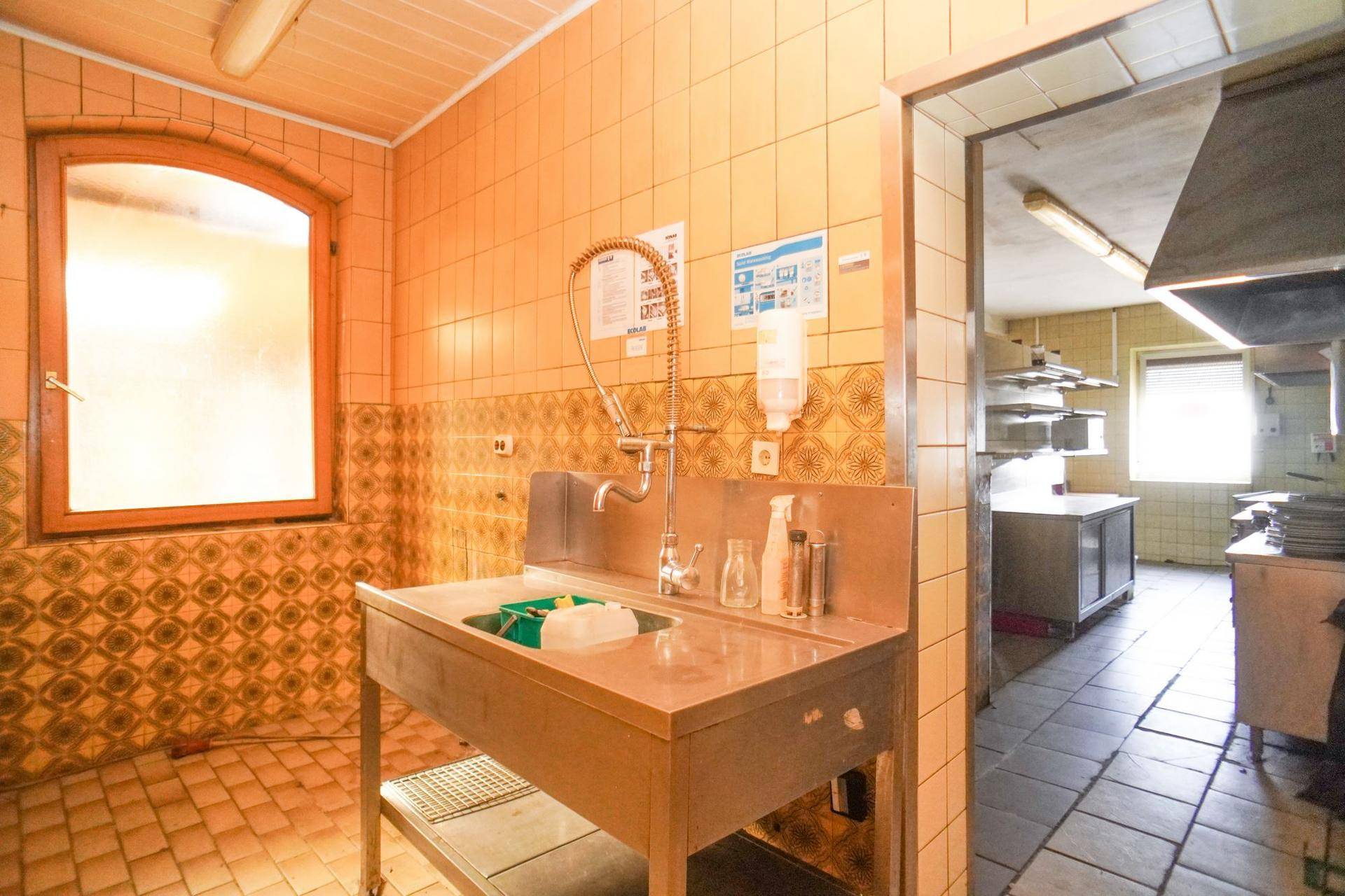 Gewerbliche Spülküche mit Edelstahlspüle, gefliesten Wänden und Bogenfenster.