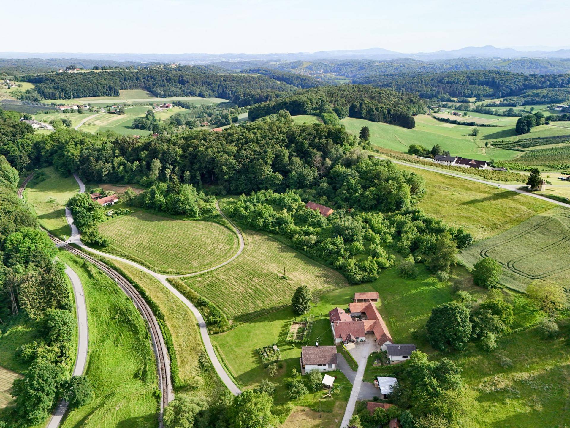 Weitläufige ländliche Ansicht mit grünen Feldern, dichten Wäldern und einer Bahnlinie, umgeben von Natur.