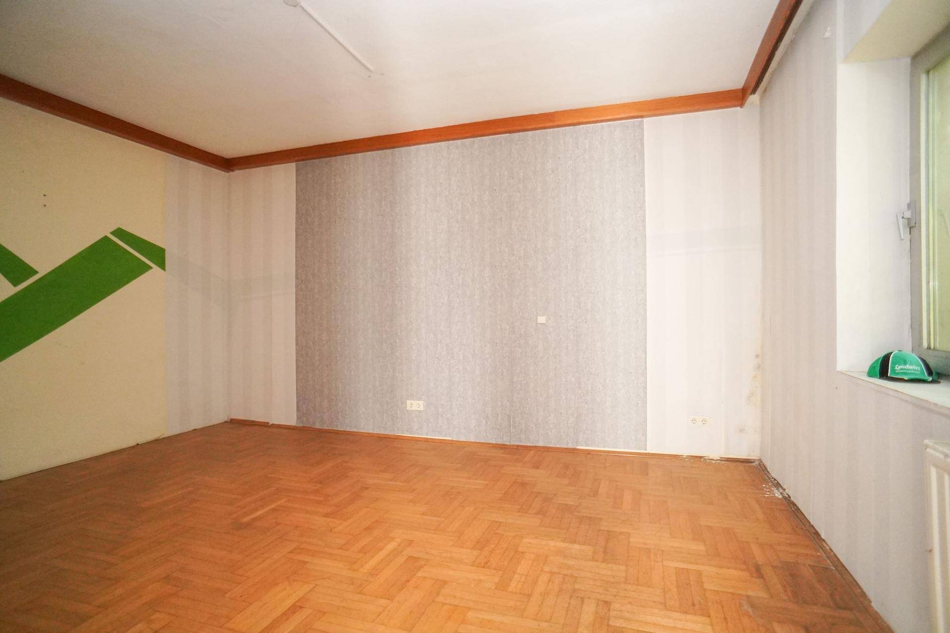 Leerer Raum mit Fischgrätparkett, Tapeten und einem Fenster.