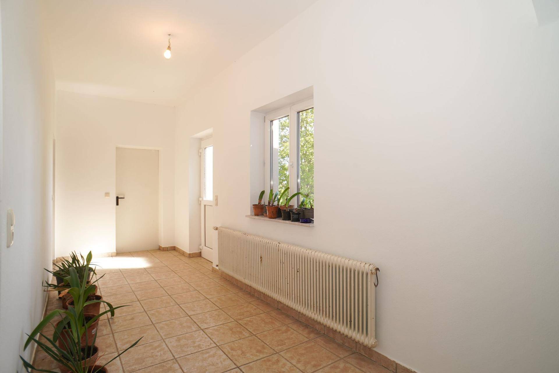 Heller Flur mit Fliesenboden, Heizkörper und Topfpflanzen am Fenster, gut gepflegt.