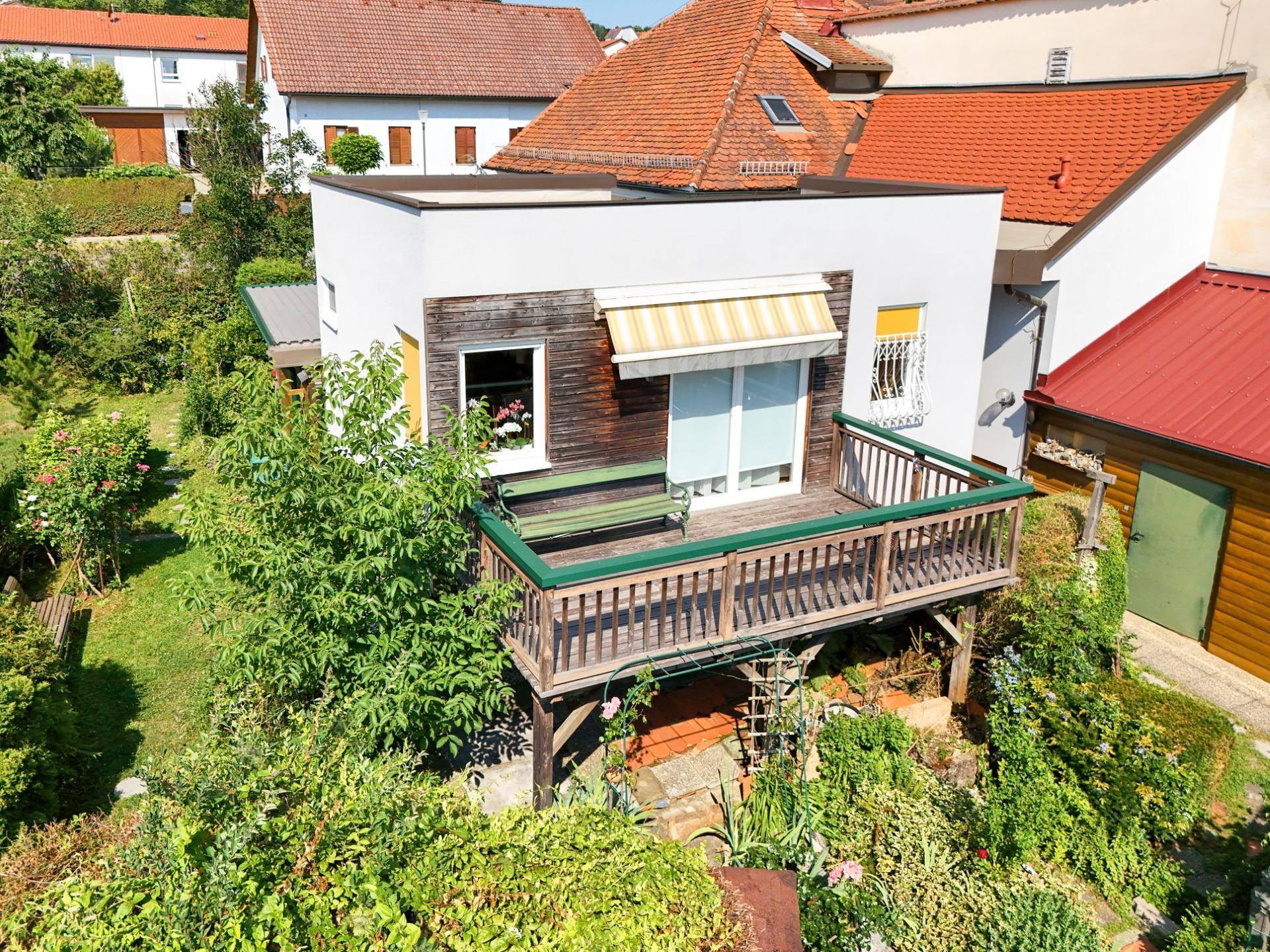 Luftaufnahme des Hauses mit einer großen Holzterrasse und Blick auf den grünen Garten.