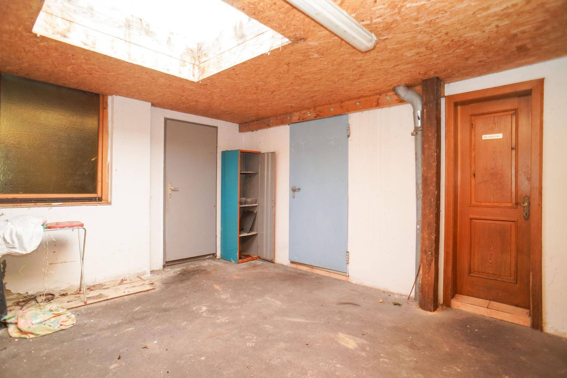 Kellerraum mit Betonboden, Holzbalken und mehreren Türen.