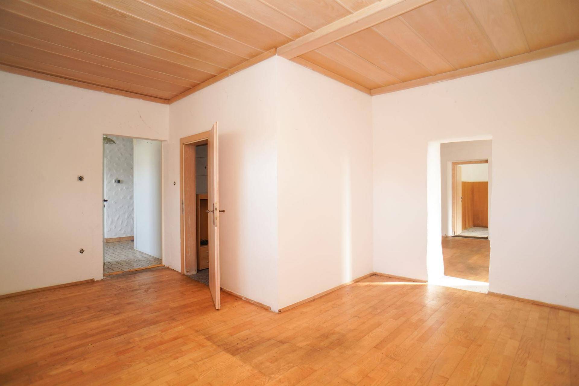 Leerer Raum mit Holzdielenboden, Holzbalkendecke und mehreren Türöffnungen.