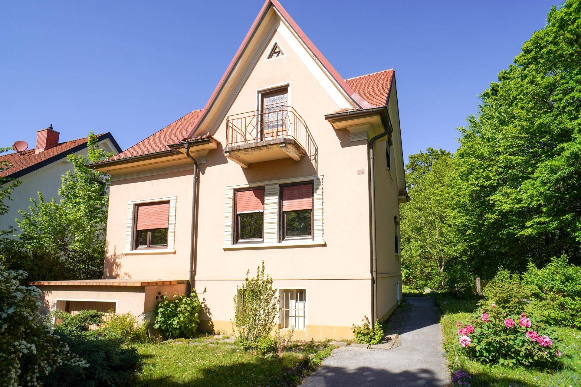 Vorderansicht des Hauses mit Balkon, rotem Dach und umgebenden Bäumen.