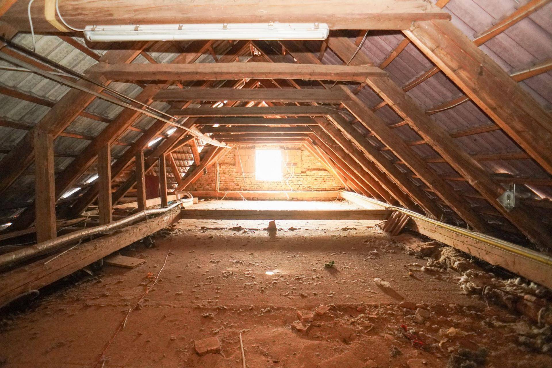 Geräumiger Dachboden mit Holzbalken, Ziegelboden und einem Fenster am Ende.