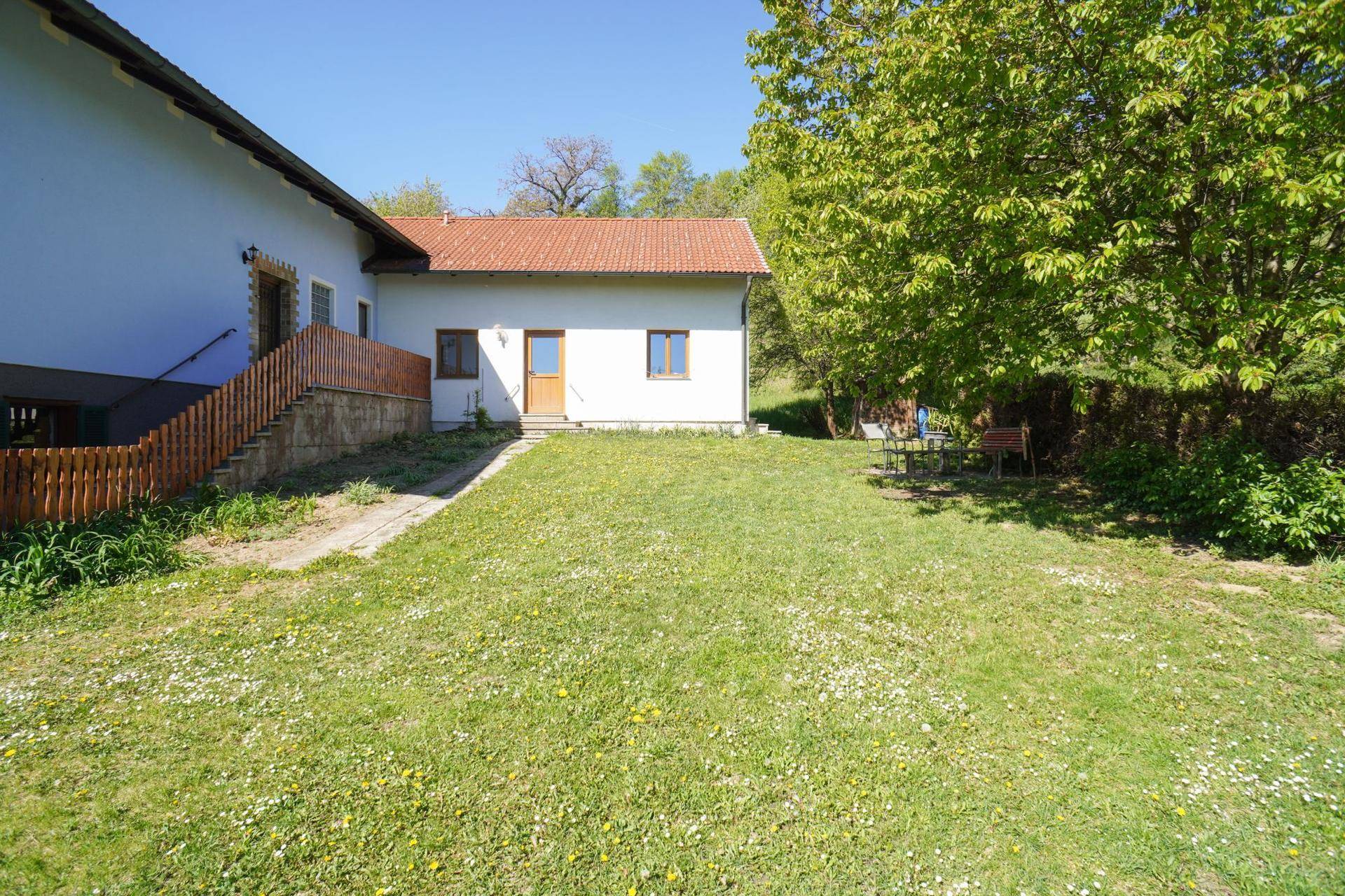 Großer Gartenbereich mit Rasenfläche, Bäumen und einem einfachen Sitzplatz im Freien.