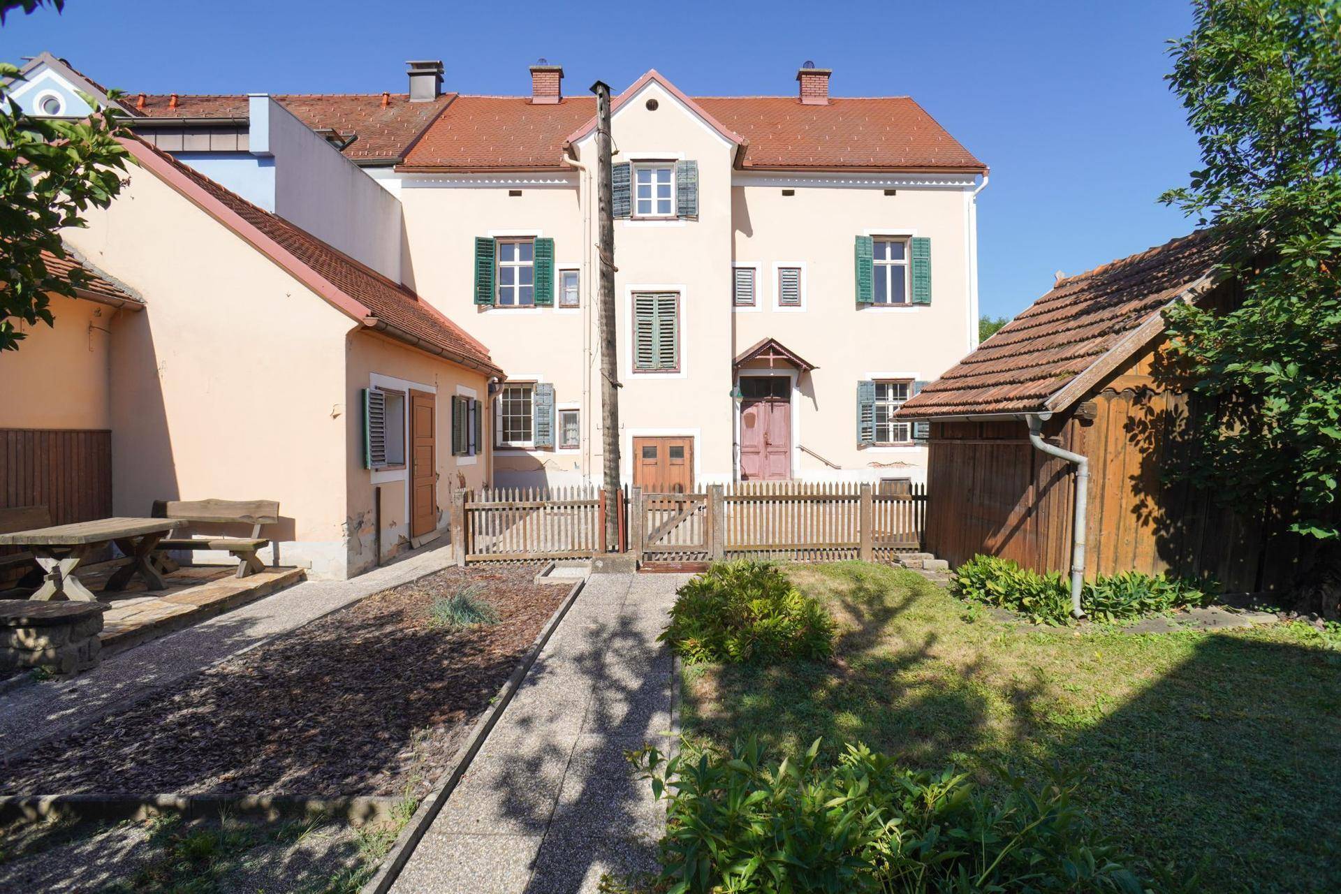 Gepflegter Gartenbereich mit Picknicktisch vor einem traditionellen Gebäude mit grünen Fensterläden.
