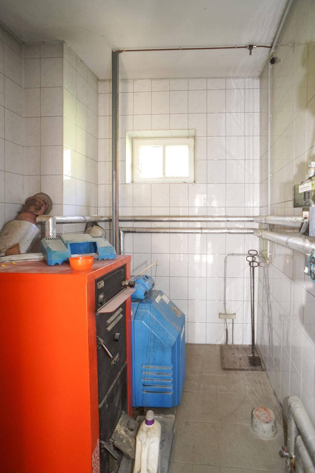 Heizungsraum mit Fliesenwänden und älterer Heizungsanlage in funktionalem Zustand.