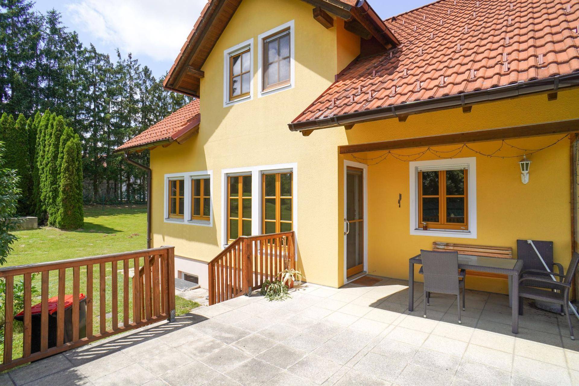 Terrasse am Haus mit Sitzgelegenheiten und Zugang zum Garten, umgeben von der gelben Fassade.