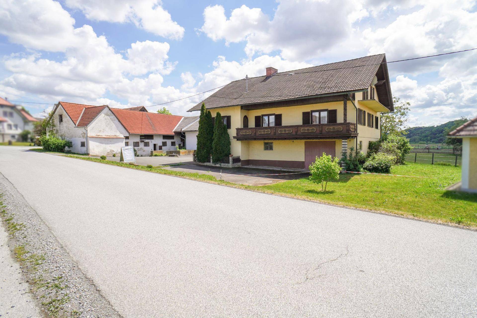 Wohnhaus mit gelber Fassade, Holzbalkon und Außentreppe, an einer ruhigen Landstraße gelegen.