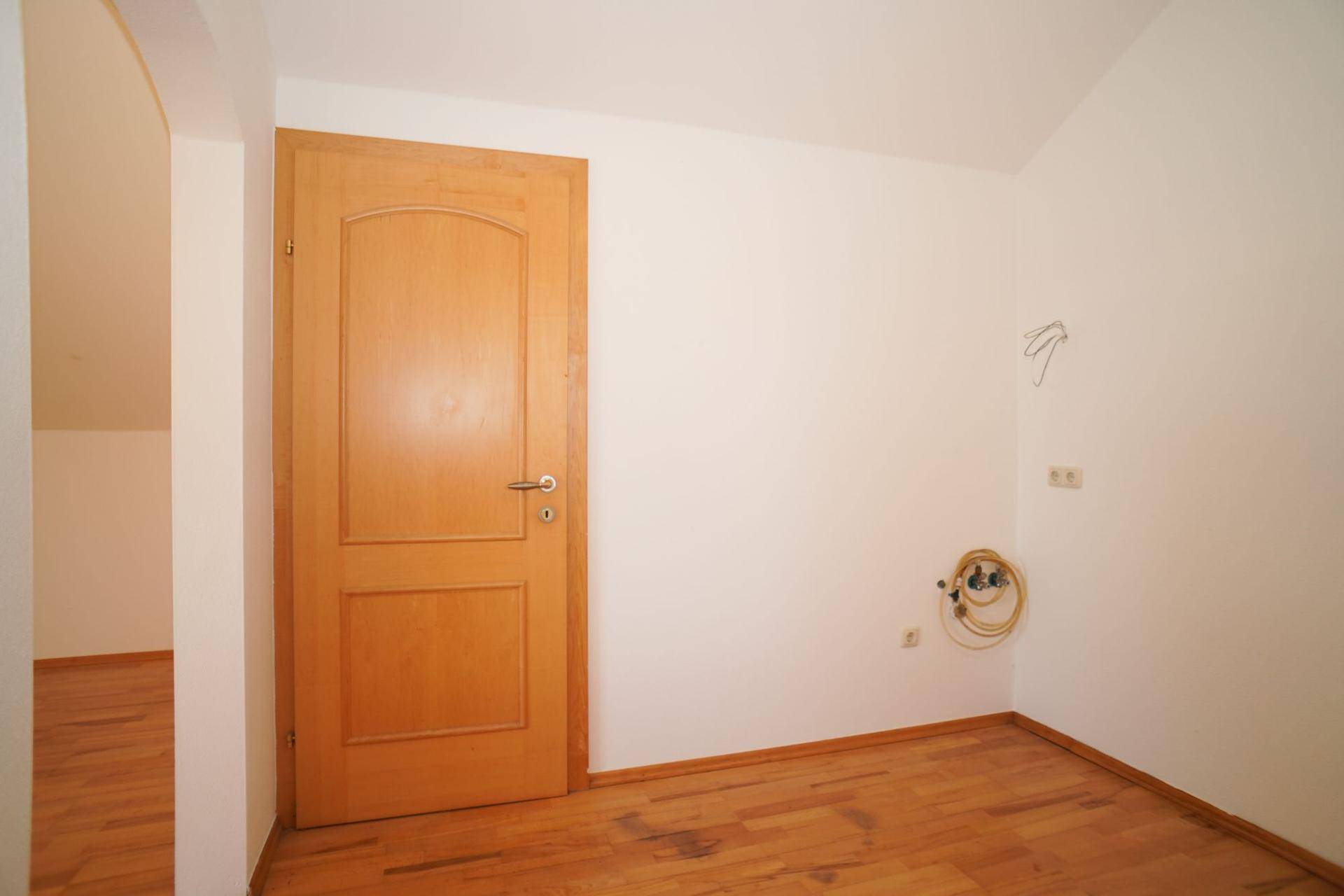 Dachzimmer mit Holzboden und Holztür, bereit für individuelle Einrichtung.