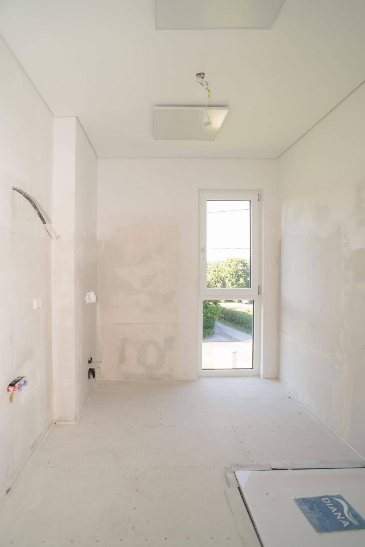 Unfertiger Raum mit Fenster und Tür zum Außenbereich, bereit für den Ausbau.