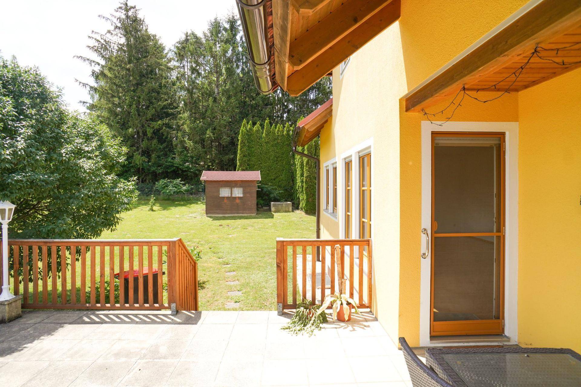 Terrasse mit Blick auf den gepflegten Garten und ein kleines Gartenhaus im Hintergrund.